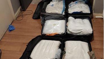 6 large plastic bags of white powder in black suitcases on a brown wooden floor.