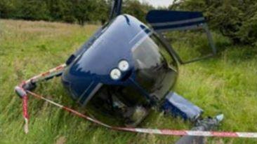 A crashing helicopter laying on its side in a field of grass