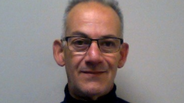 A mug shot Philippos Economides who is stood with his arm crossed and wearing a navy sweater. He has short silver hair and is clean shaven. He is lightly smiling.