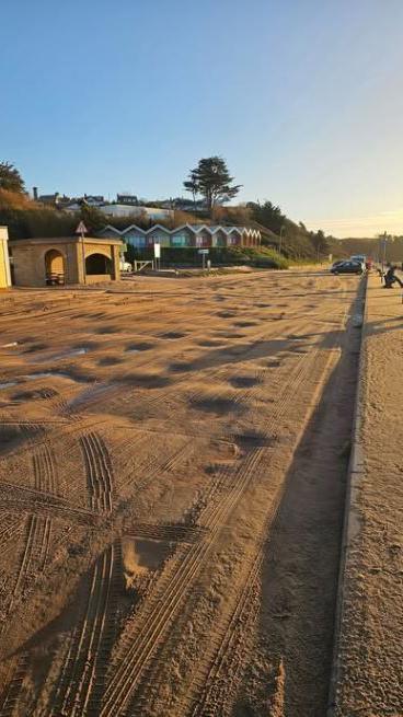 A seafront covered with sand and some beach huts in the distance.