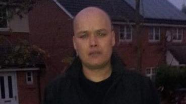 Crash victim Kevin Bishop standing in front of a row of houses in a black jacket looking at a camera