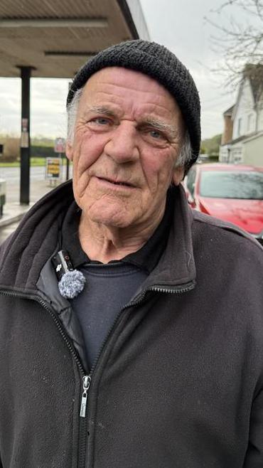 Man in black fleece and hat standing in a forecourt