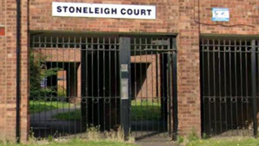 The front of a three-storey block of flats. There is a white sign with black writing that reads "Stoneleigh Court" and black metal gates in the middle of the first floor. 