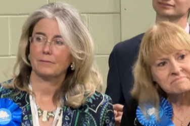 Two women look on as results come in. They have blue Conservative rosettes on. 