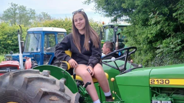 Mali Picton-Jones ar y fferm yn eistedd ar gerbyd amaethyddol