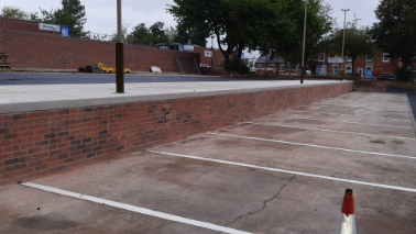 Rows of newly created parking spaces with housing and buildings in the background.