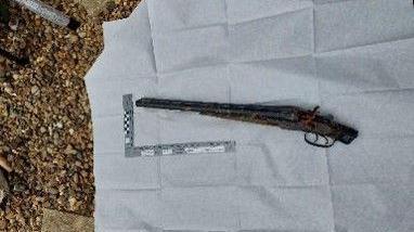 A black shotgun has been put on the ground and sits on top of a white sheet. 