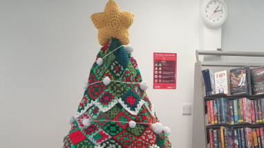 the star on top of a crocheted Christmas tree next to a bookshelf in a library