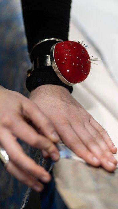 A close up of a woman's hand pressing down the seam of some fabric, wearing a red pin cushion on her wrist.