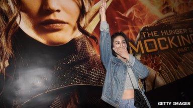 Woman uses three finger salute in front of Hunger Games movie poster