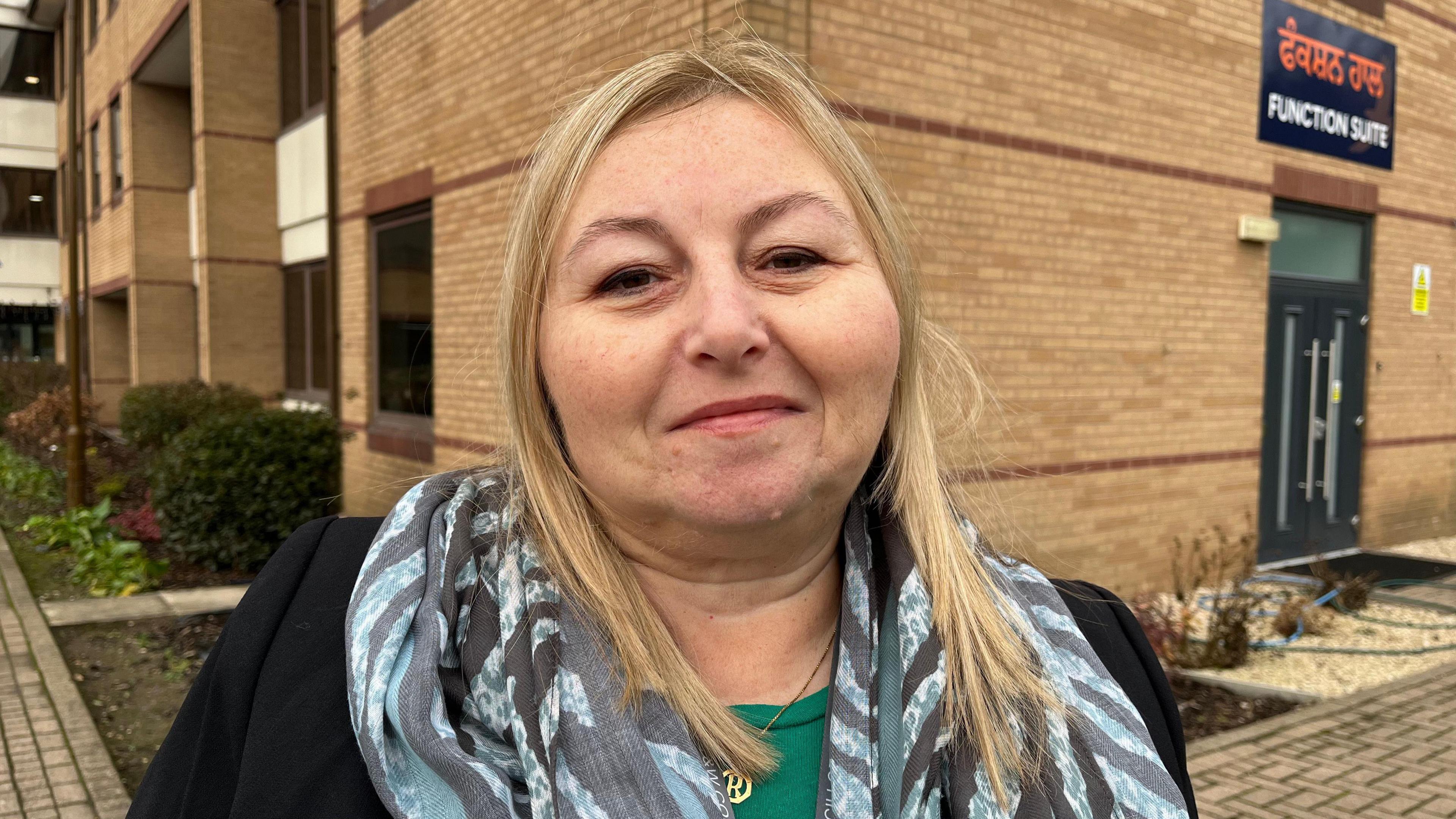 Councillor Rachael Tyrrell with shoulder length blonde hair. She is wearing a blue and black zebra print scarf, a black blazer and a green t-shirt underneath.