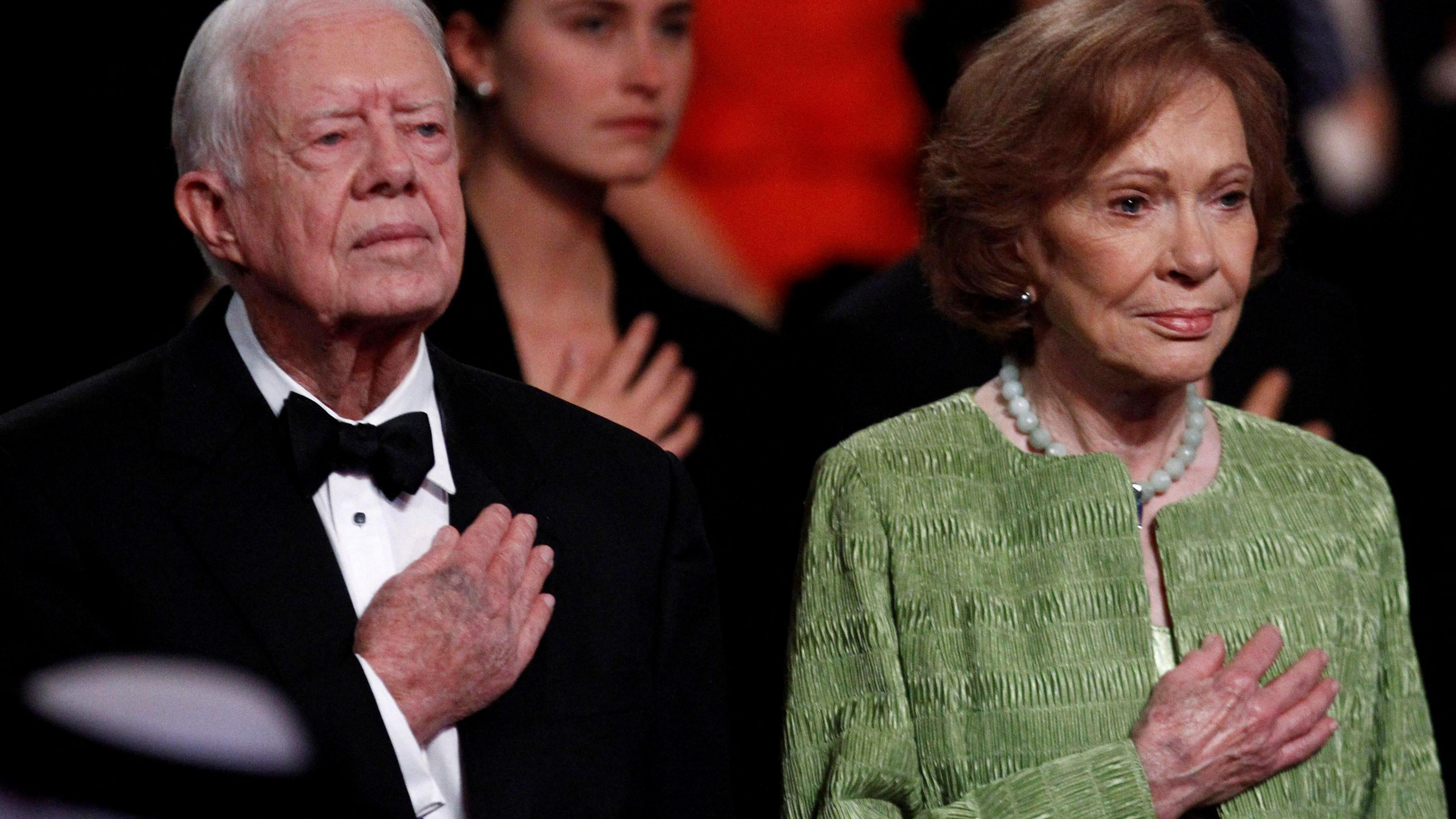 Former U.S. President Jimmy Carter and his wife Rosalynn hold their right hands on their chests at a ceremony