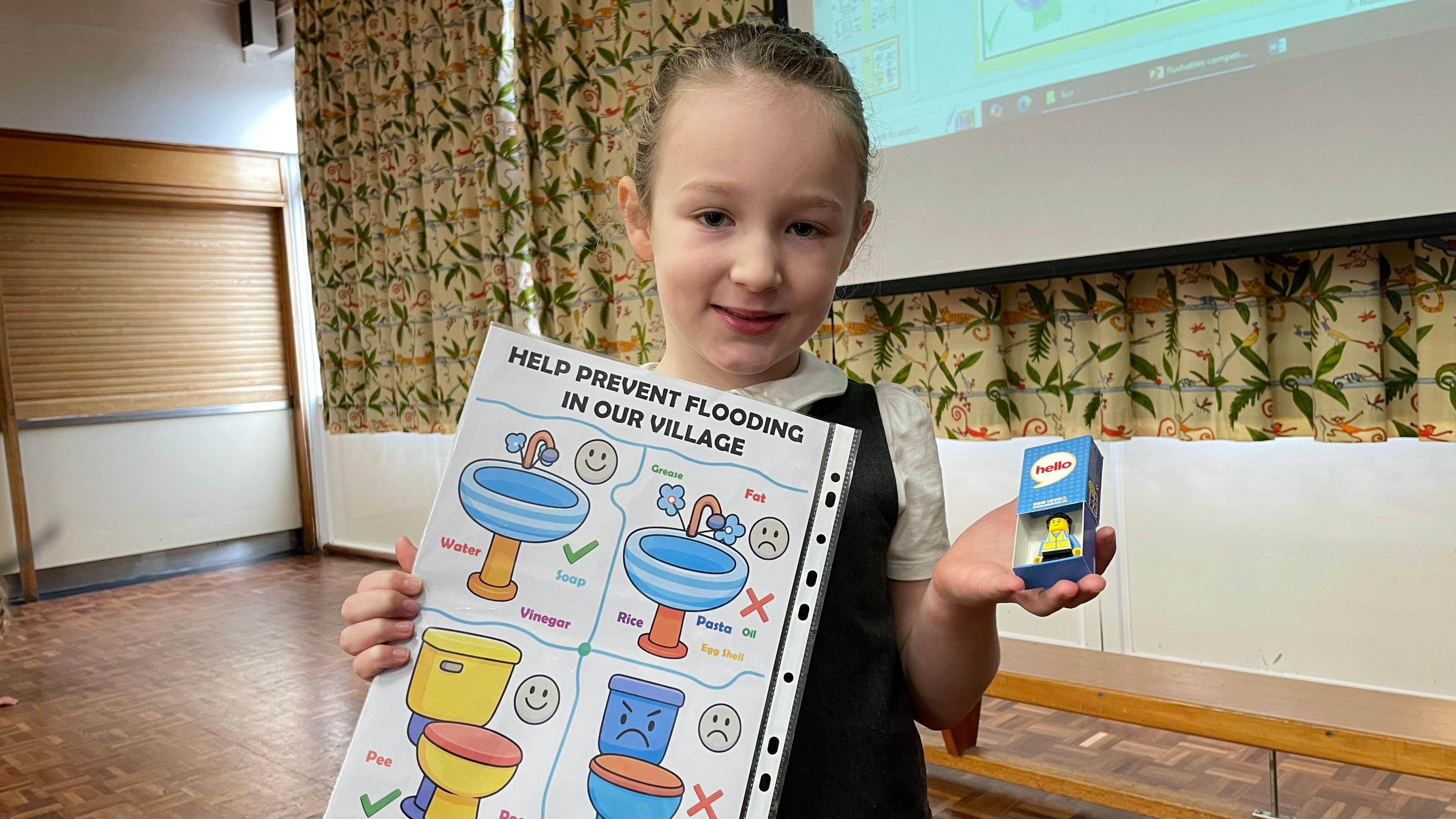 A girl holding a poster in one hand and a Lego figurine in the other. She is smiling at the camera.