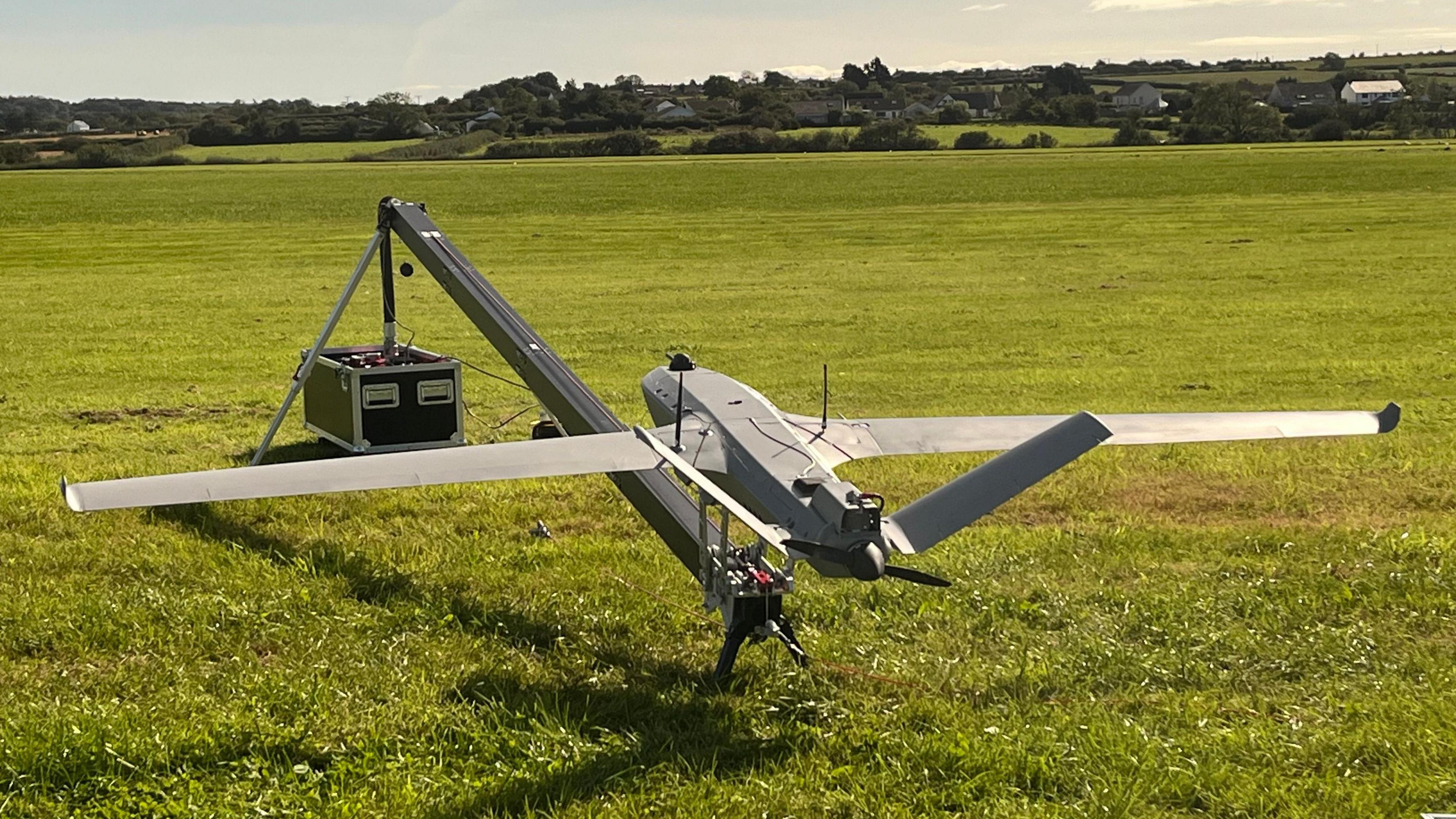 A Tekever AR3 drone, which is shaped like a plane with large wings and a tail, in a field