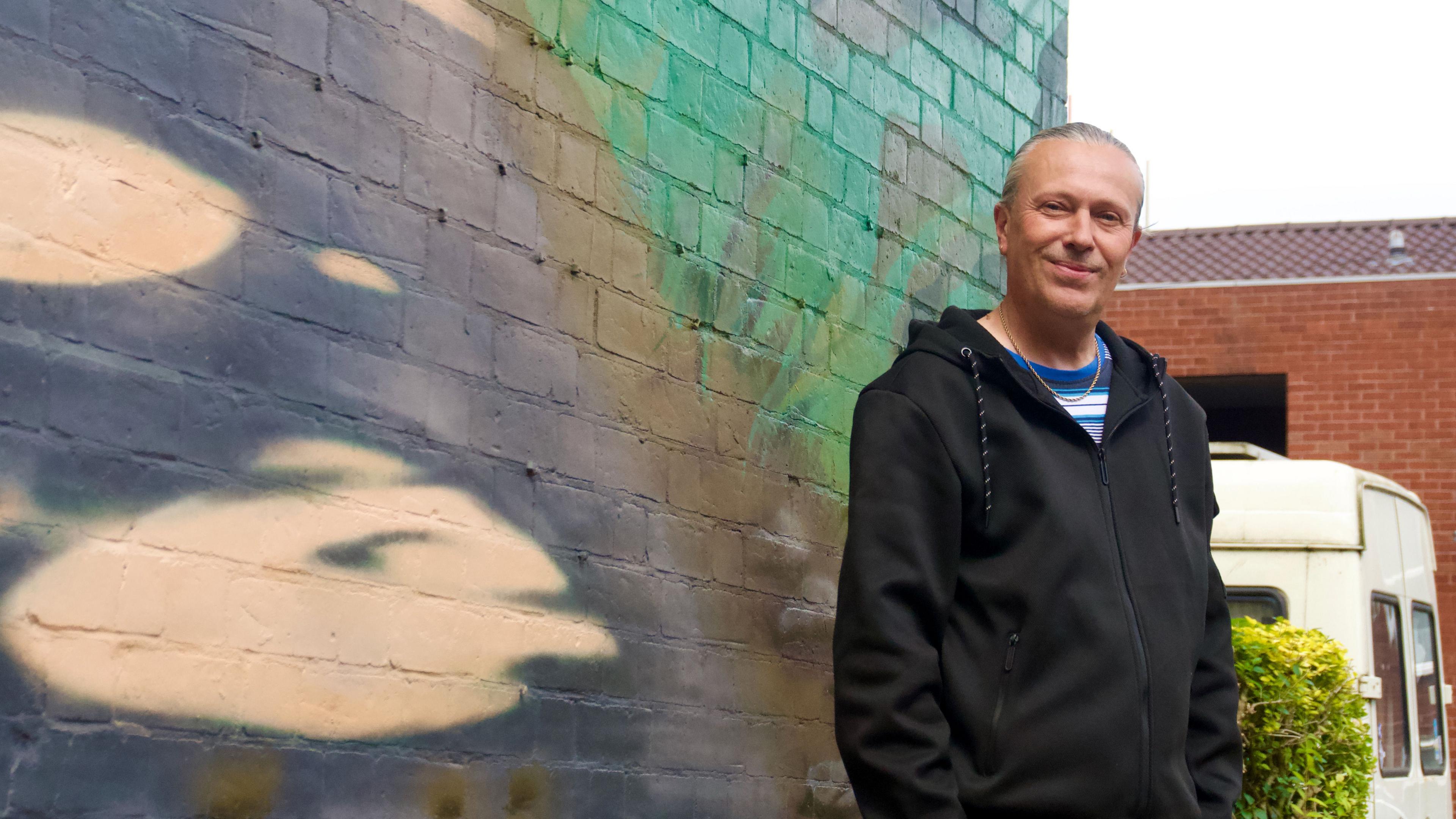 Man next to mural being painted on side of house