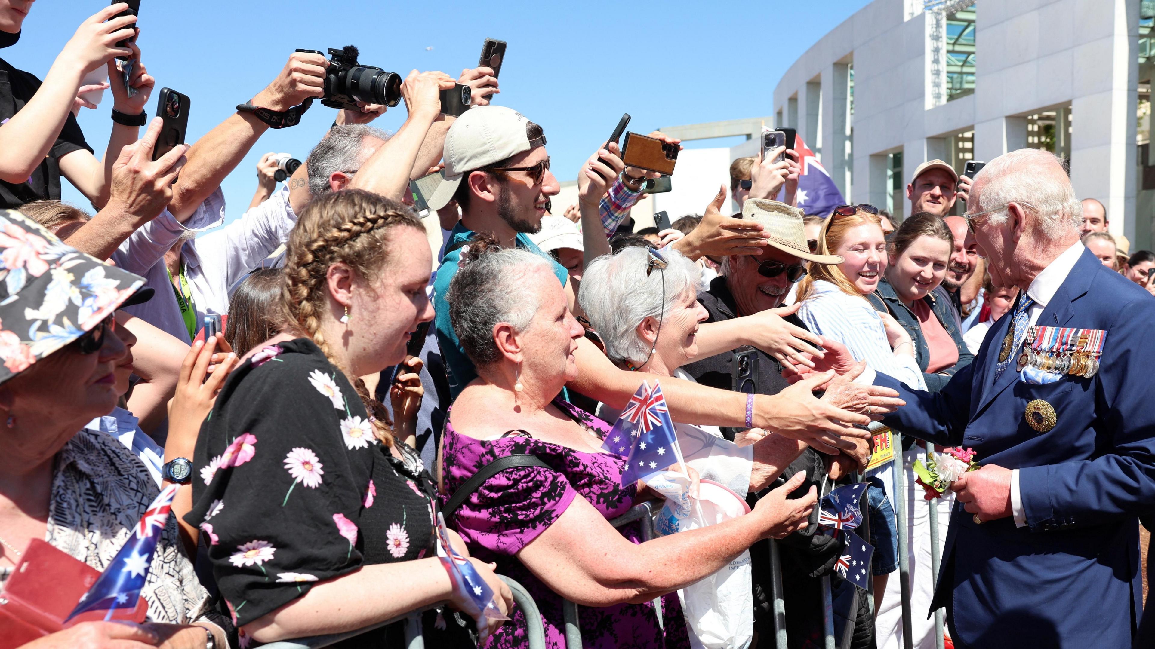 Crowds wave Australian flags and hold up phones to take pictures as 