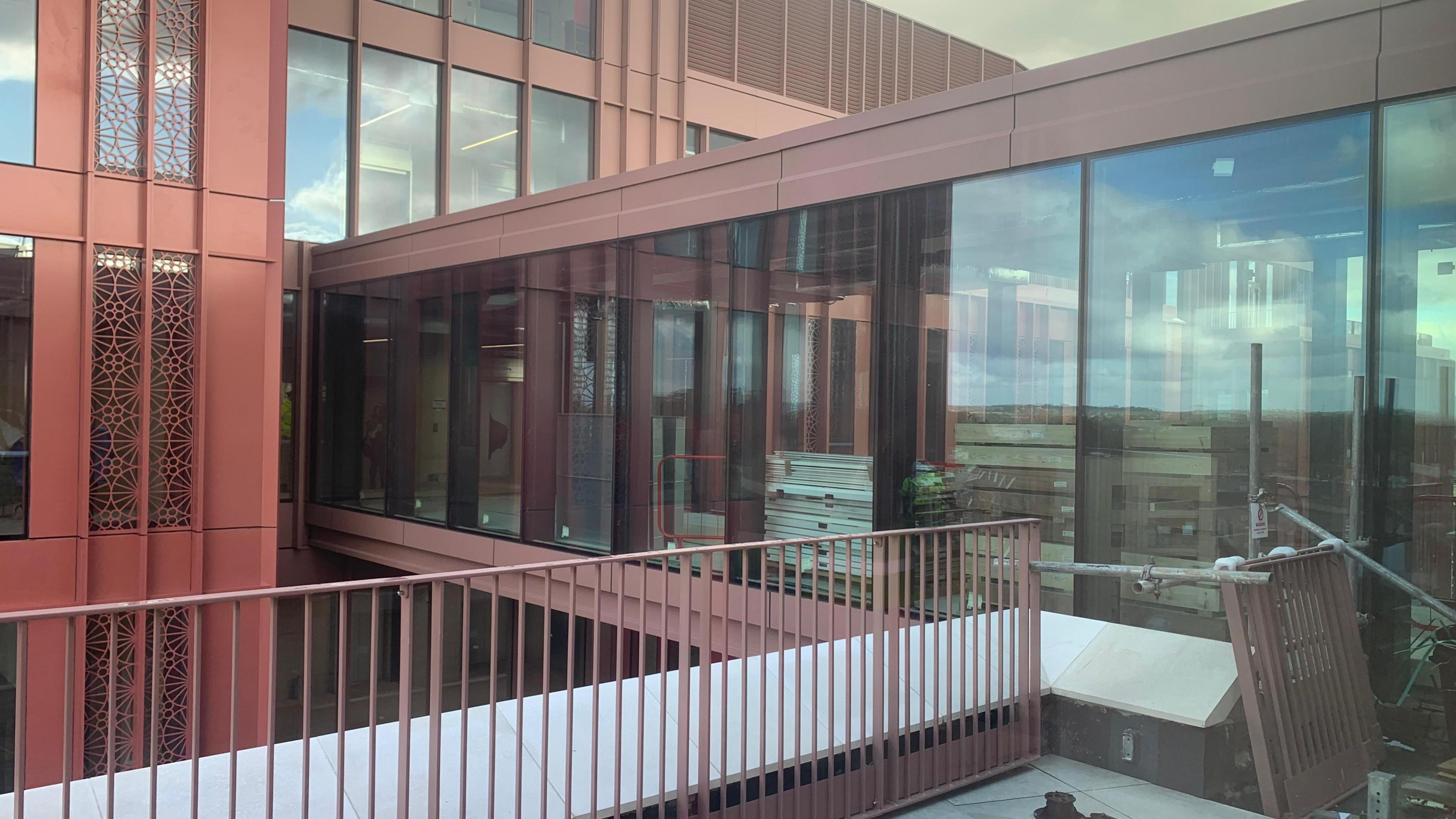 The bridge outside the new Forum building. The facade is red and it includes full length glass windows.