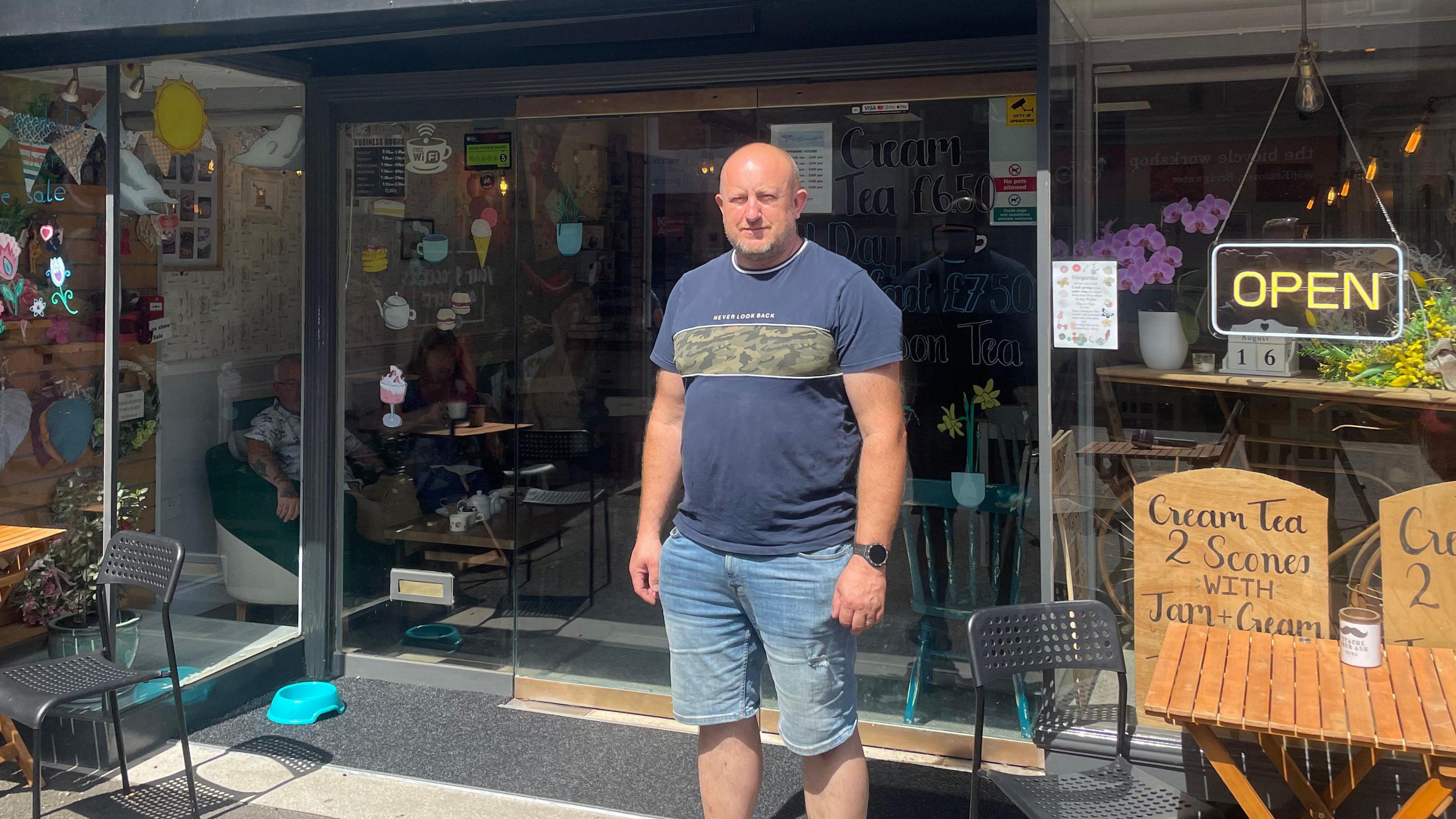 Mario Gogolin stands outside the Cafe Margeritka in Bridgwater. There is a sign in the window which says 'Open' and also signs advertising cream teas. 