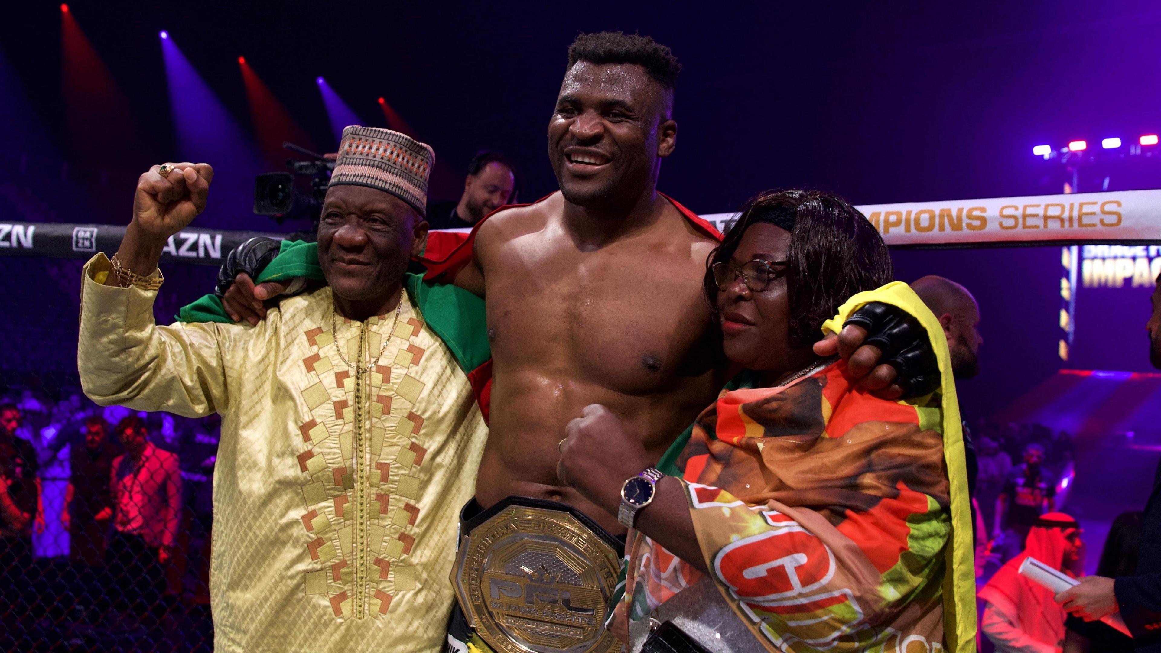 Francis Ngannou is pictured smiling in the octagon while wearing a championship MMA belt and with his arms around two relatives who are holding up their fists