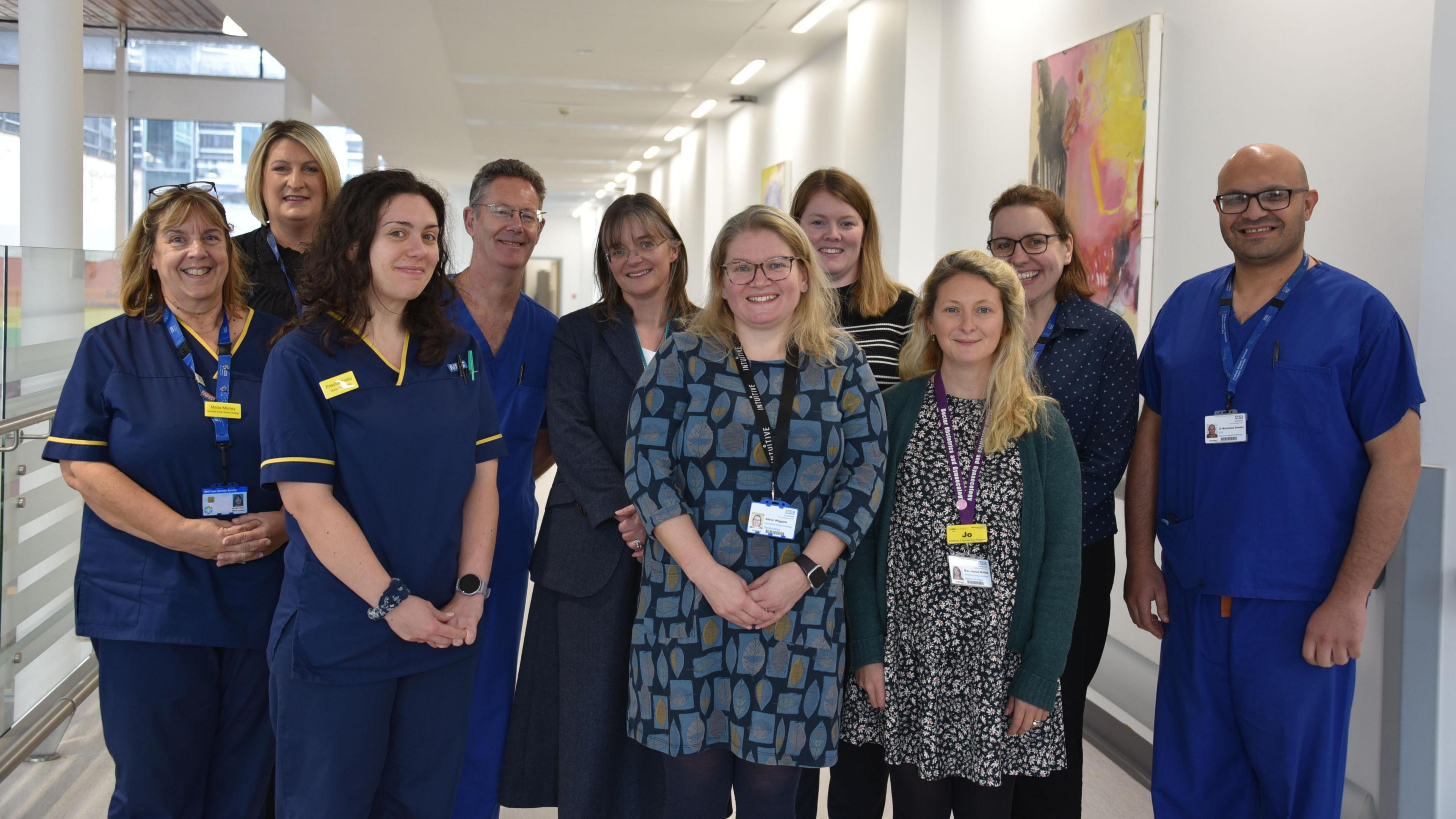 Ten members of staff in Somerset NHS Foundation Trust’s gynaecological-oncology team. They are wearing blue scrubs and some five are wearing office work attire. They are all wearing ID badges and you can see what looks like a hospital corridor in the background.