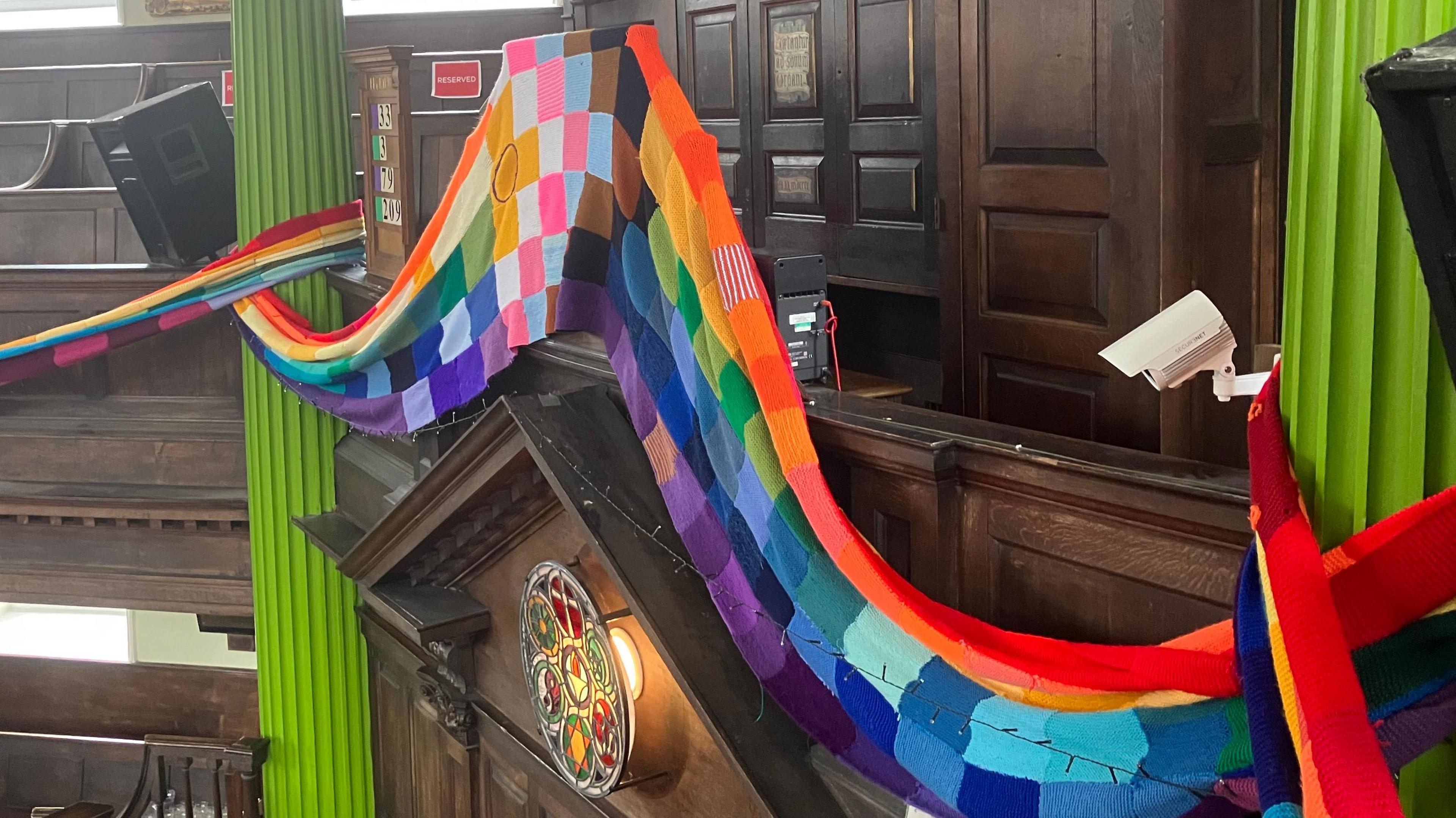 The pride flag scarf, wrapped around the Octogen Chapel in Norwich. In the middle, there are panels featuring the progress flag.