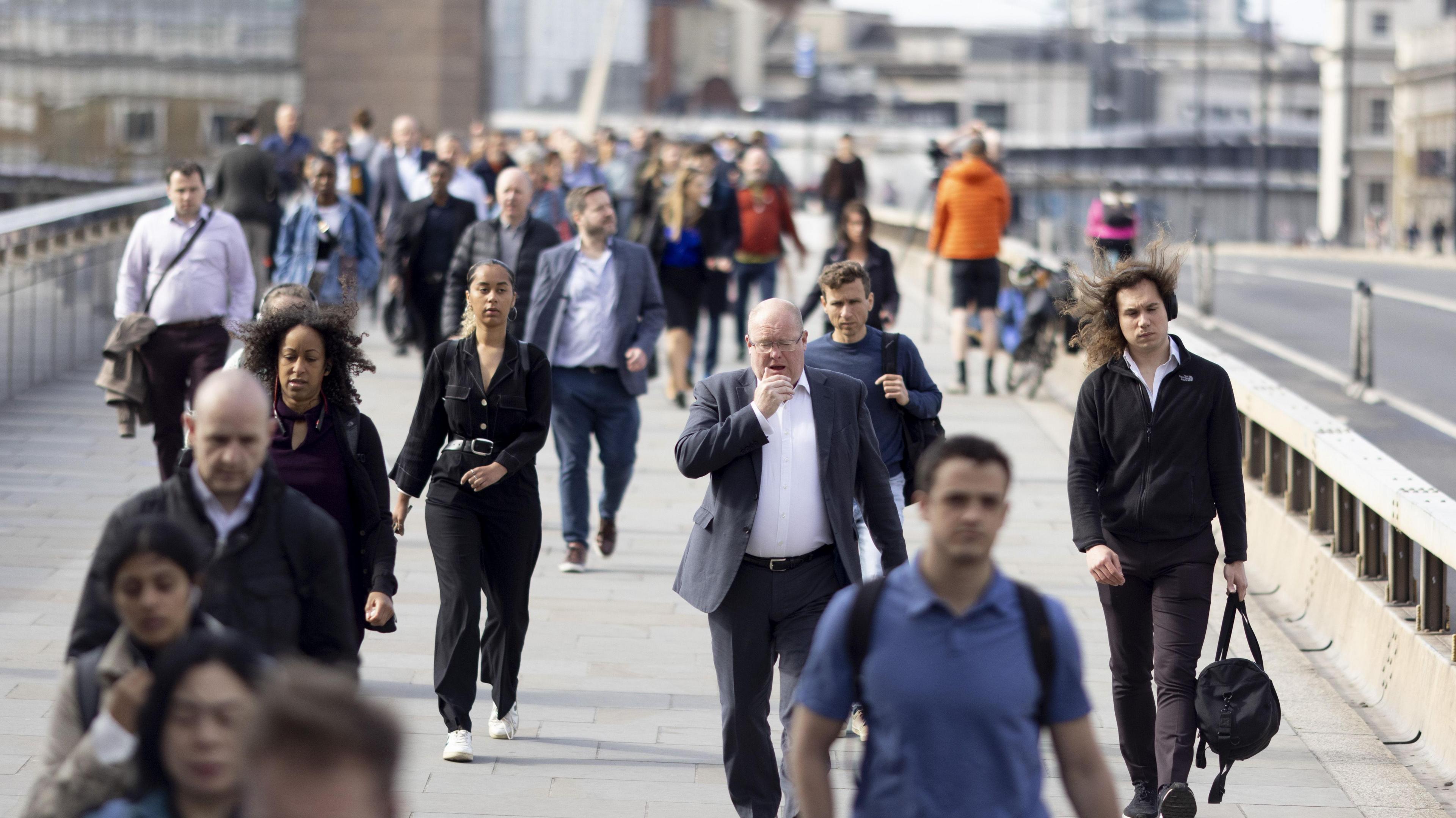People in suits and casual outfits walk across a bridge on a sunny day.