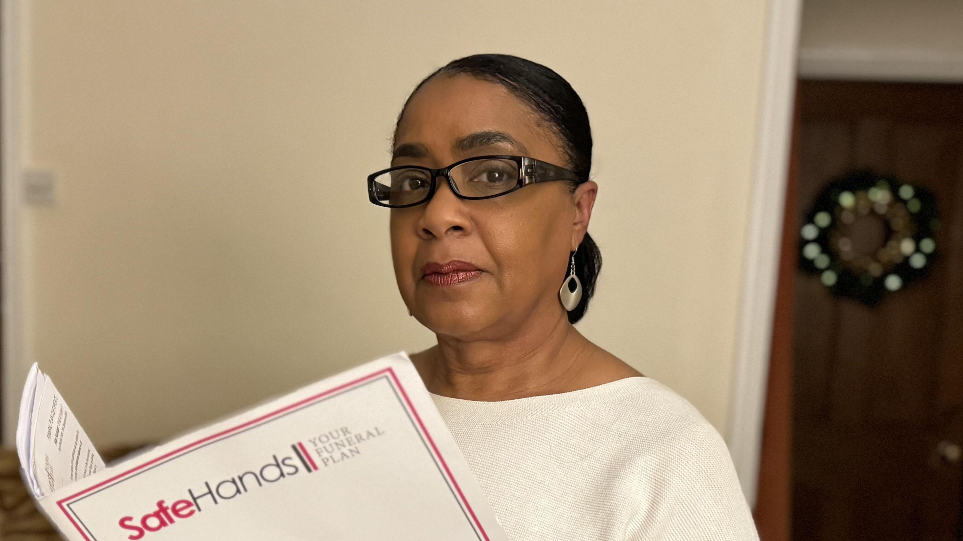 A woman wearing a white jumper and glasses holding a folder with Safe Hand branding.