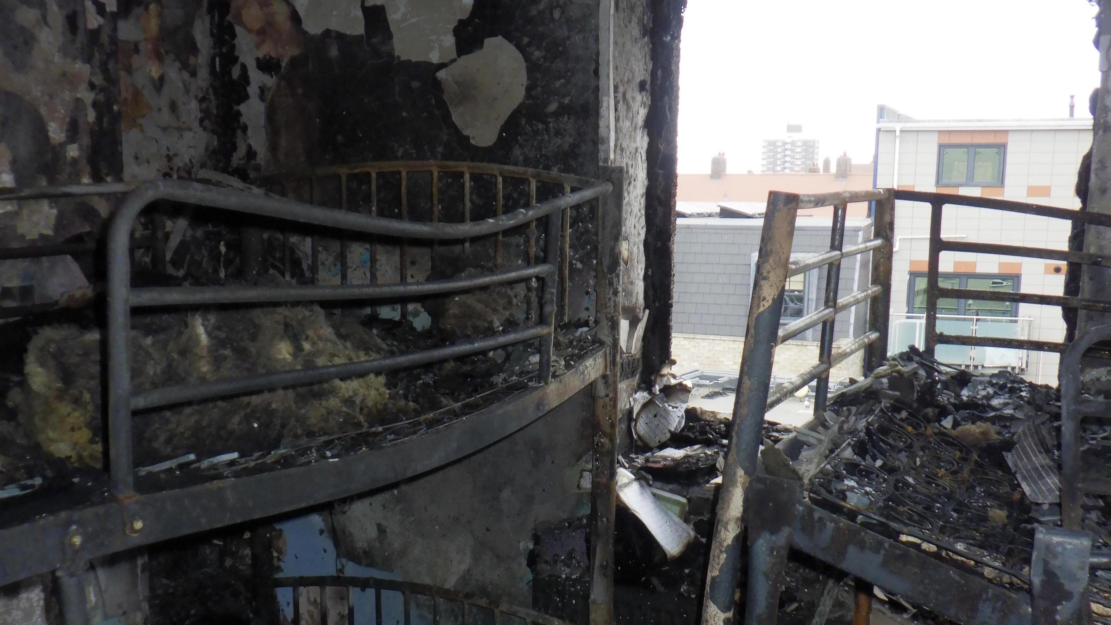 The burnt interior of one of the rooms, with multiple charred metal bed frames. 