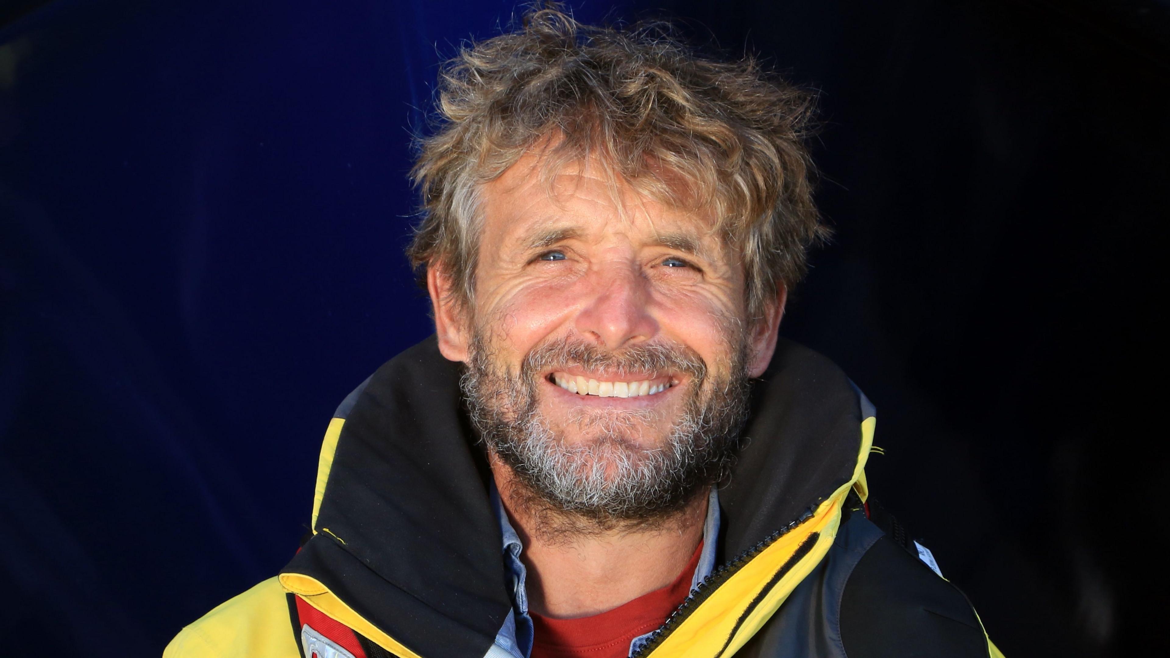 RNLI Sennen Cove Duty Coxswain Kirstan Gorvin. He's wearing a black and yellow coat and is smiling at the camera. He has mousey coloured hair and a grey, black and brown beard.