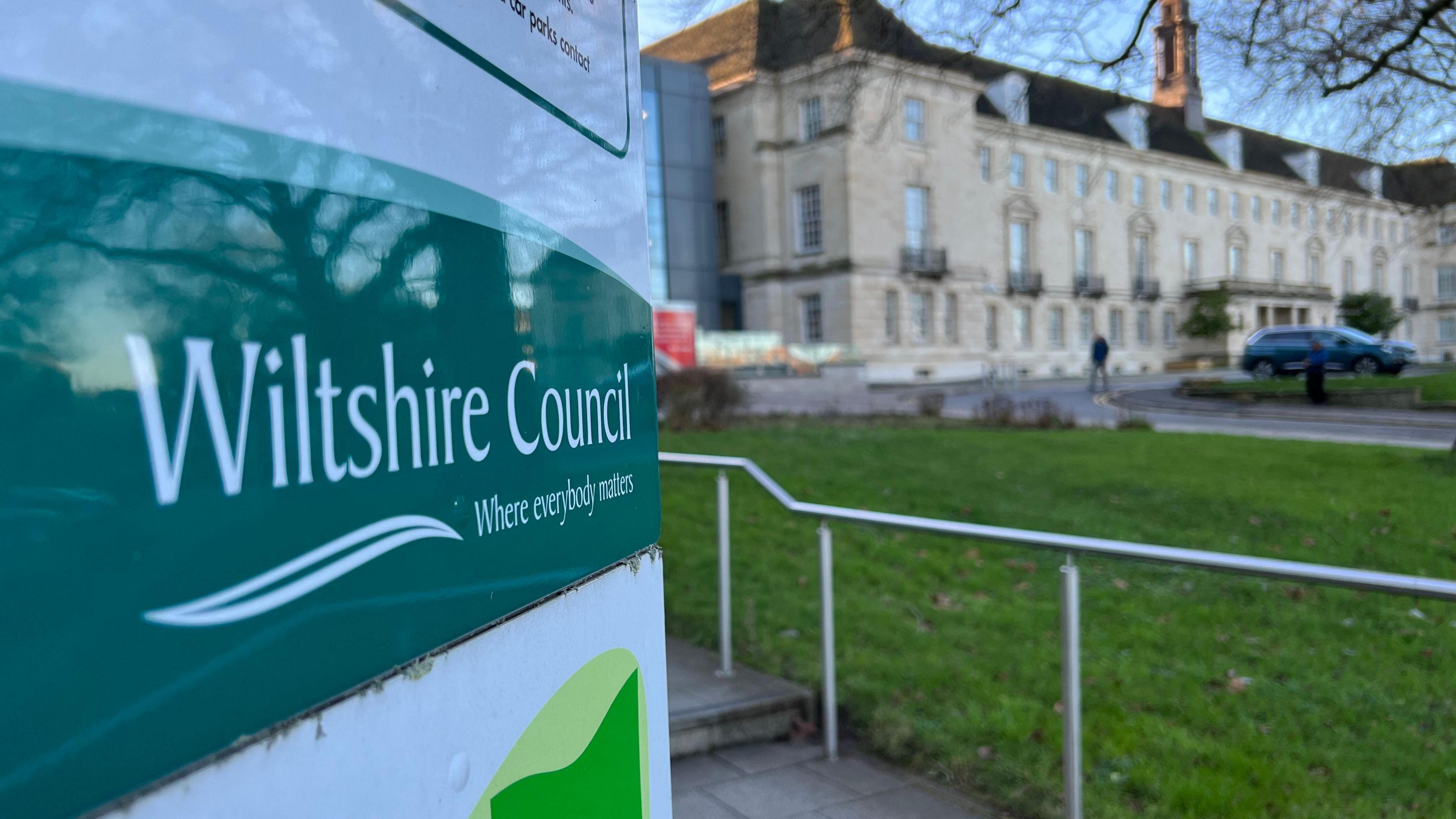 An exterior view of Wiltshire Council's building with a sign bearing the council's name in the foreground