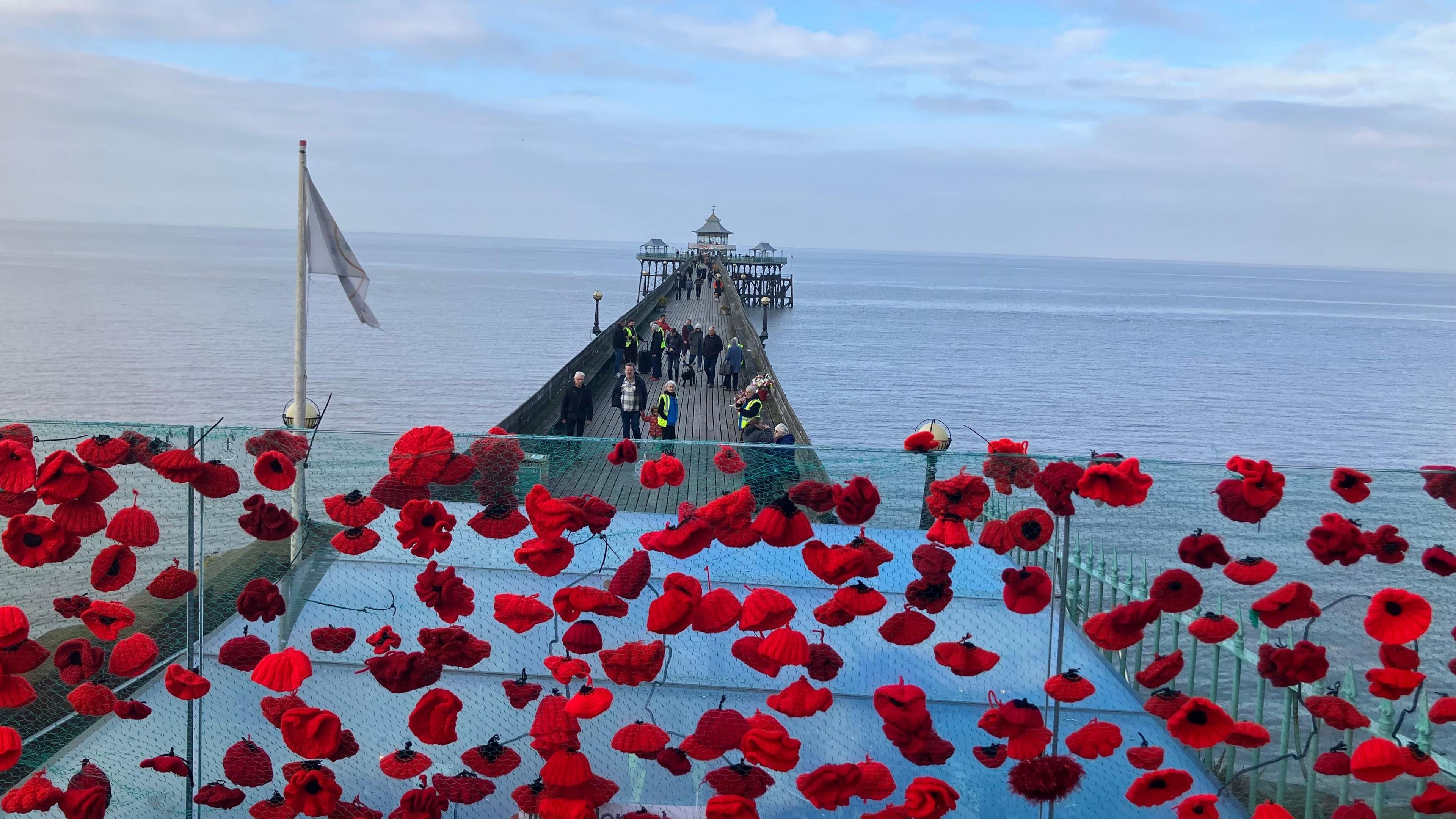 Handmade poppies attached to a wire fence overlooking Clevedon's pier.