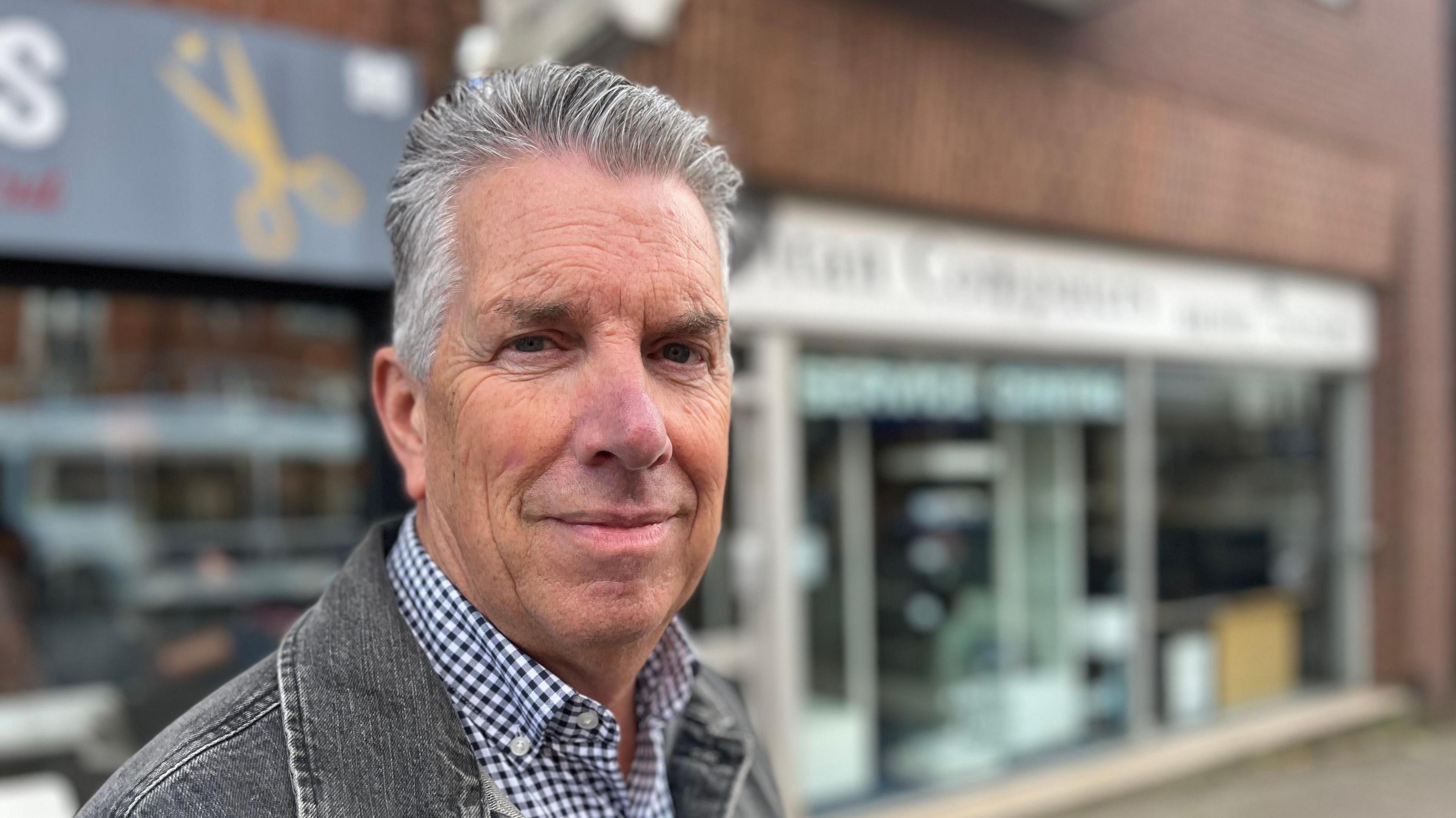 Phil Bowler, owner of Titan Computers, wearing a check shirt and faded black denim jacket, with the Titan Computers shop in a blurred background