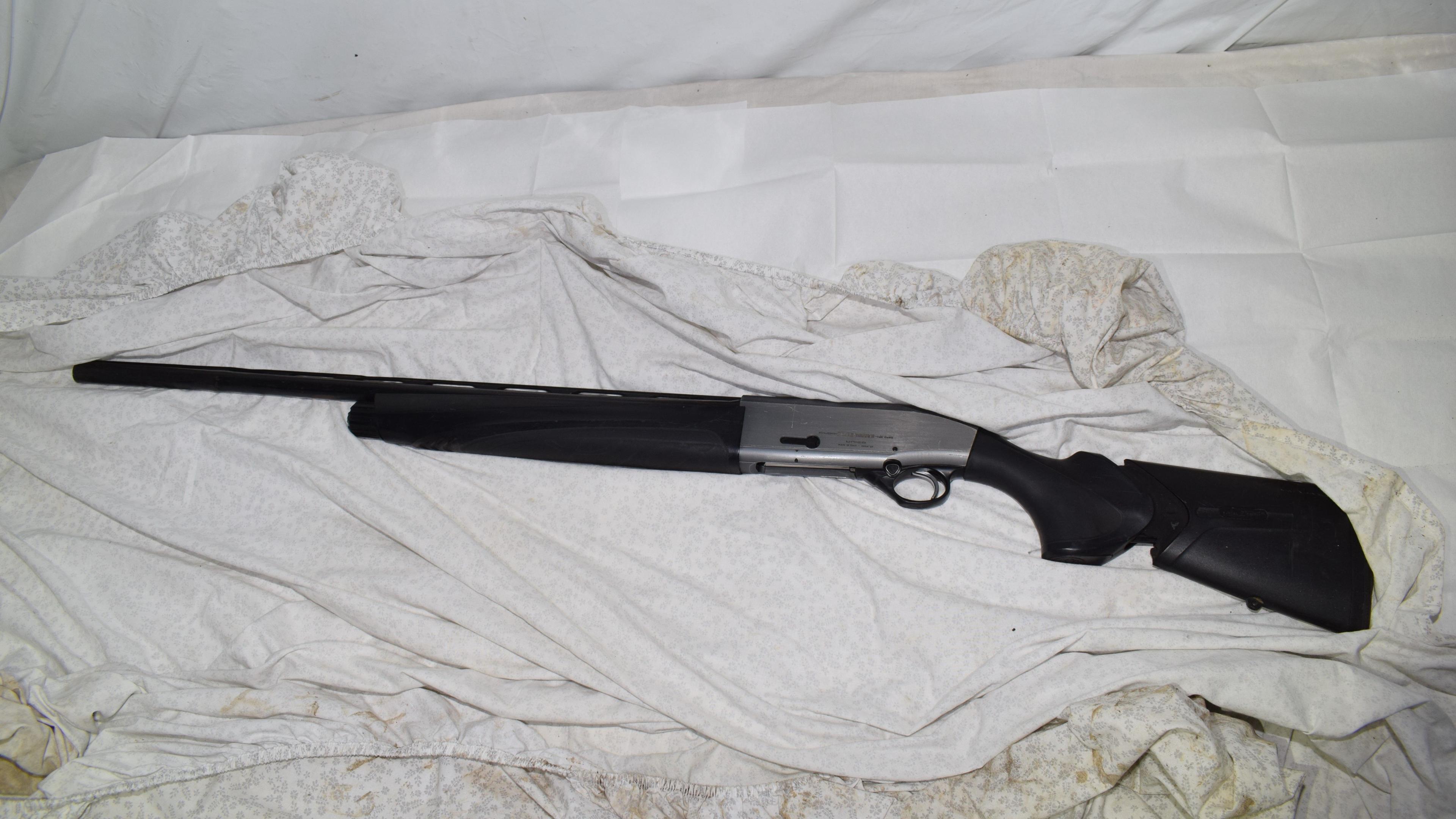 A shotgun lying on untidy bed covers.