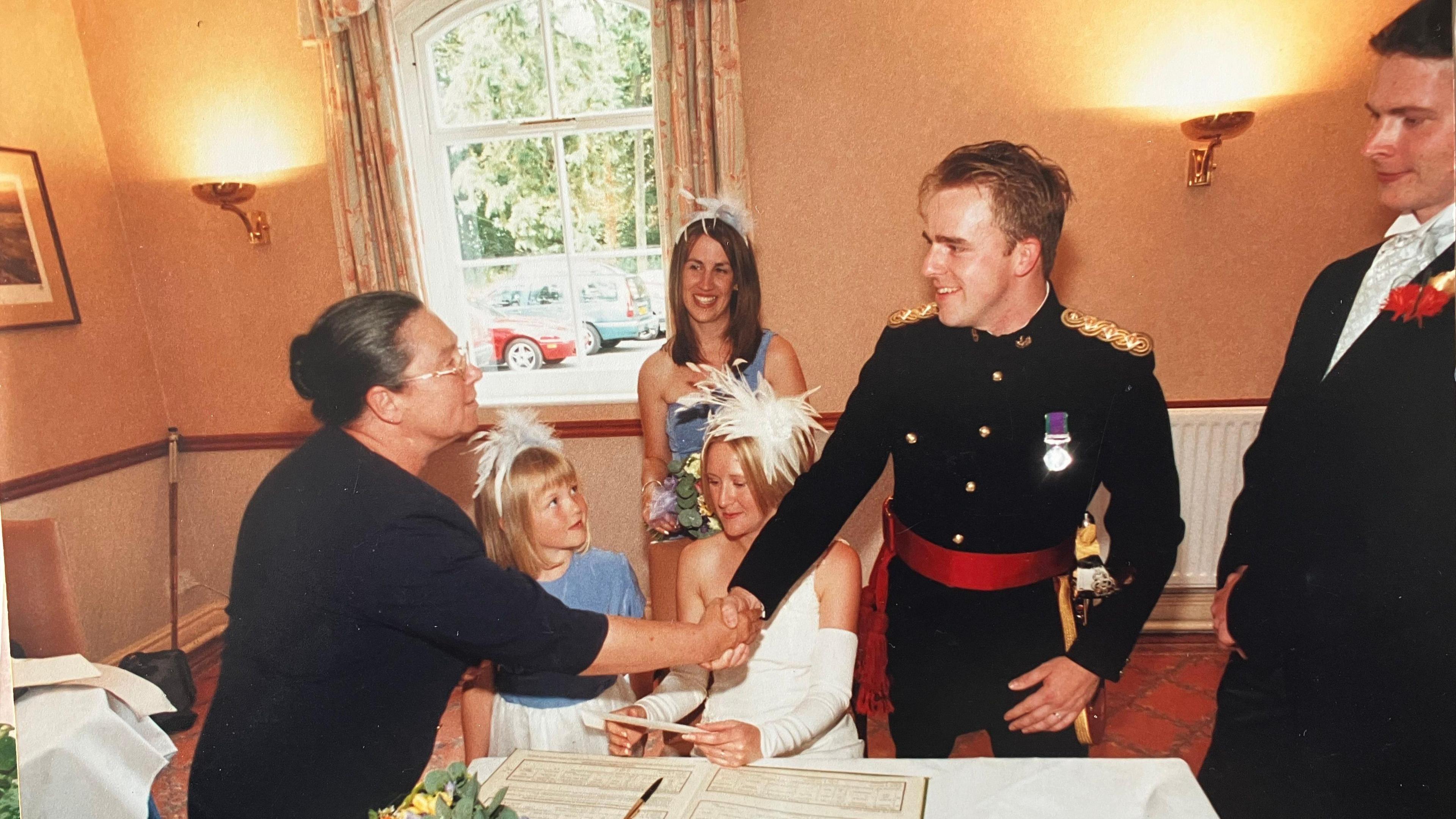 Alicia shakes the hand of a newlywed groom, dressed in military style uniform.