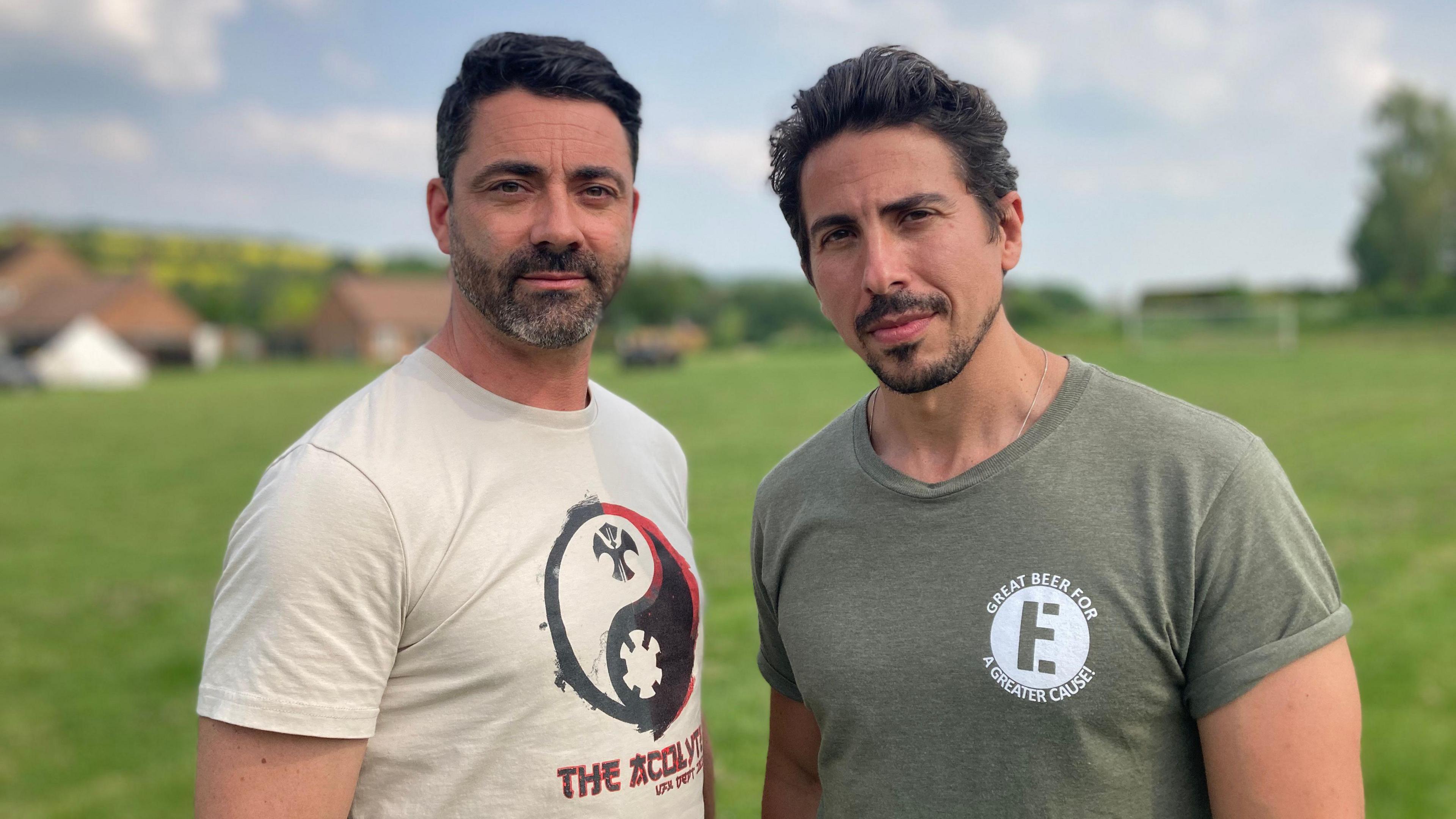 Actors Alex Sagba-Brady and Christian Black look at the camera while standing in the Aldbourne playing field