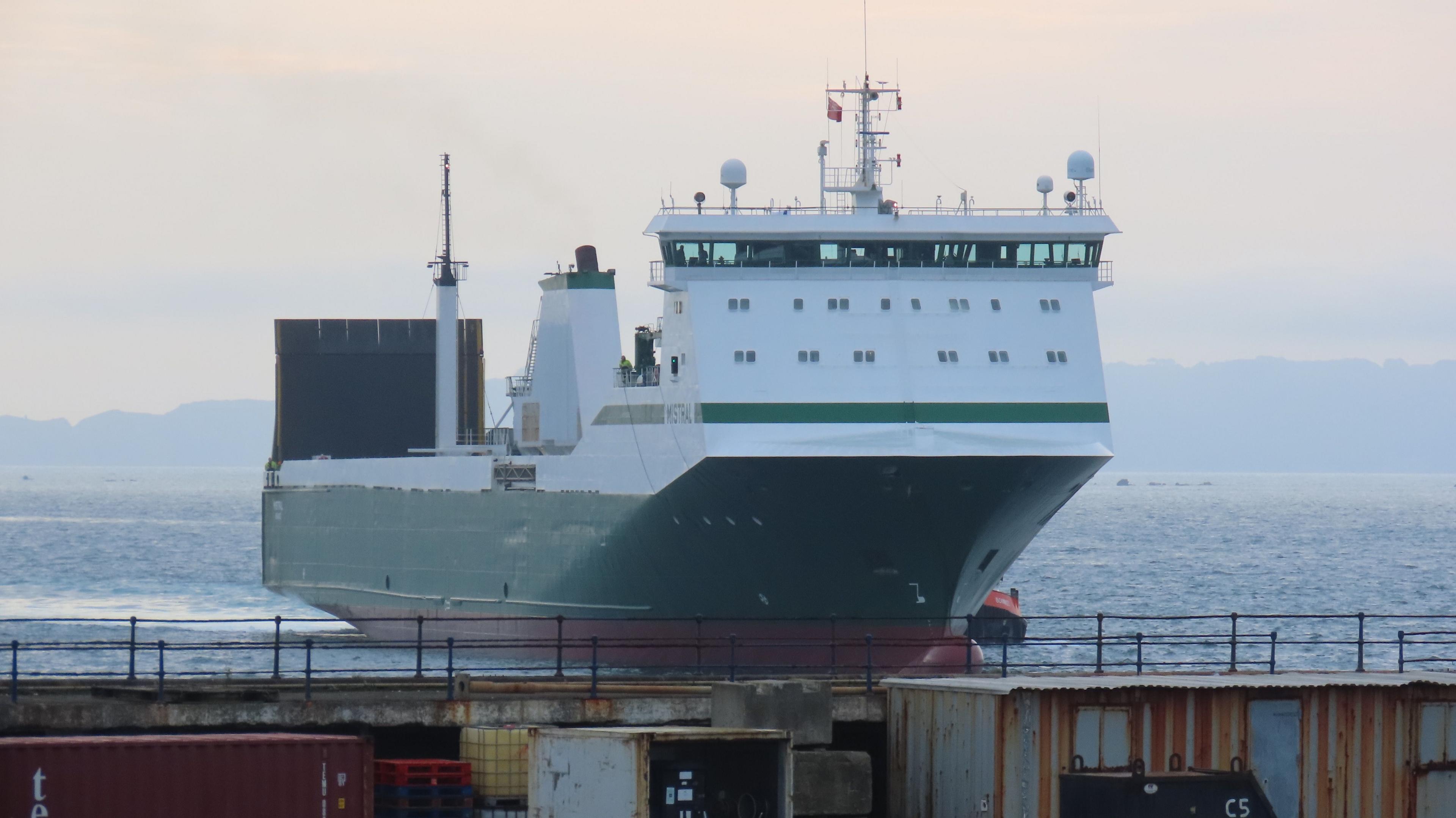 A ship with a green hull and a white cabin approaching St Peter Port Harbour over the railing. 