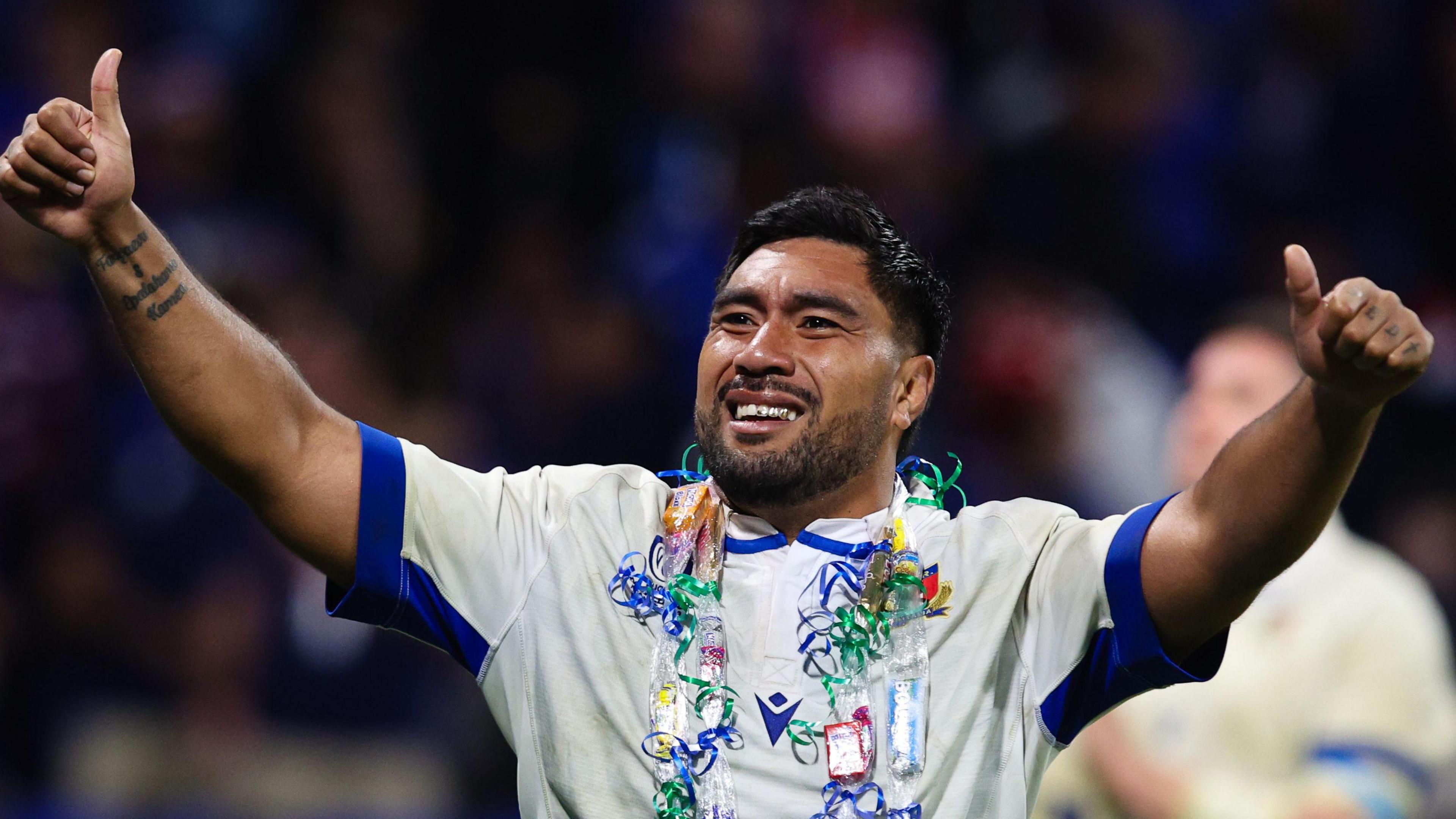 Hame Faiva wearing a white Italy kit with thumbs up on both hands, a big smile and daisy-chain style thing around his neck
