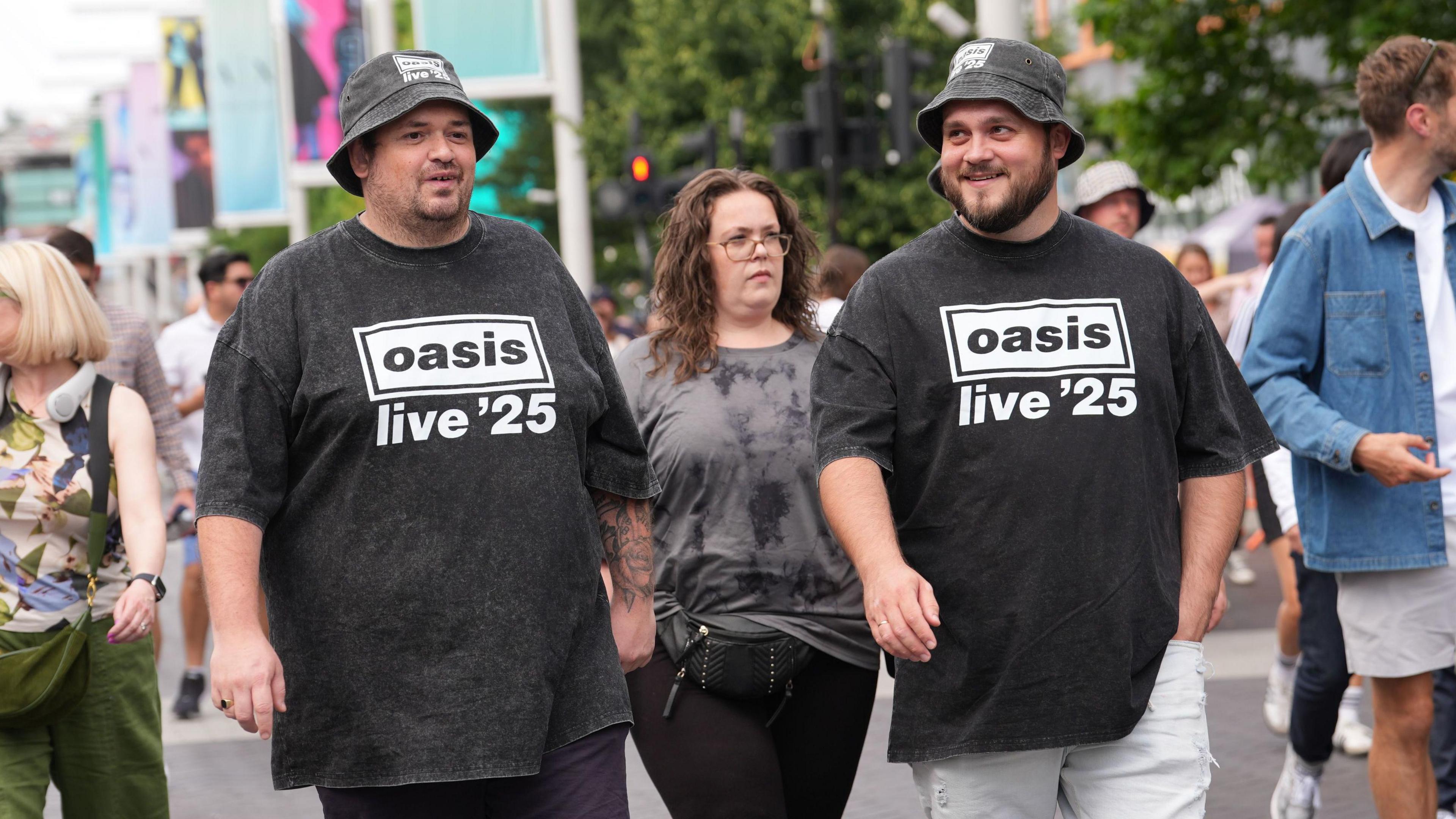 Oasis fans in black t-shirts and black bucket hats on Wembley Way.