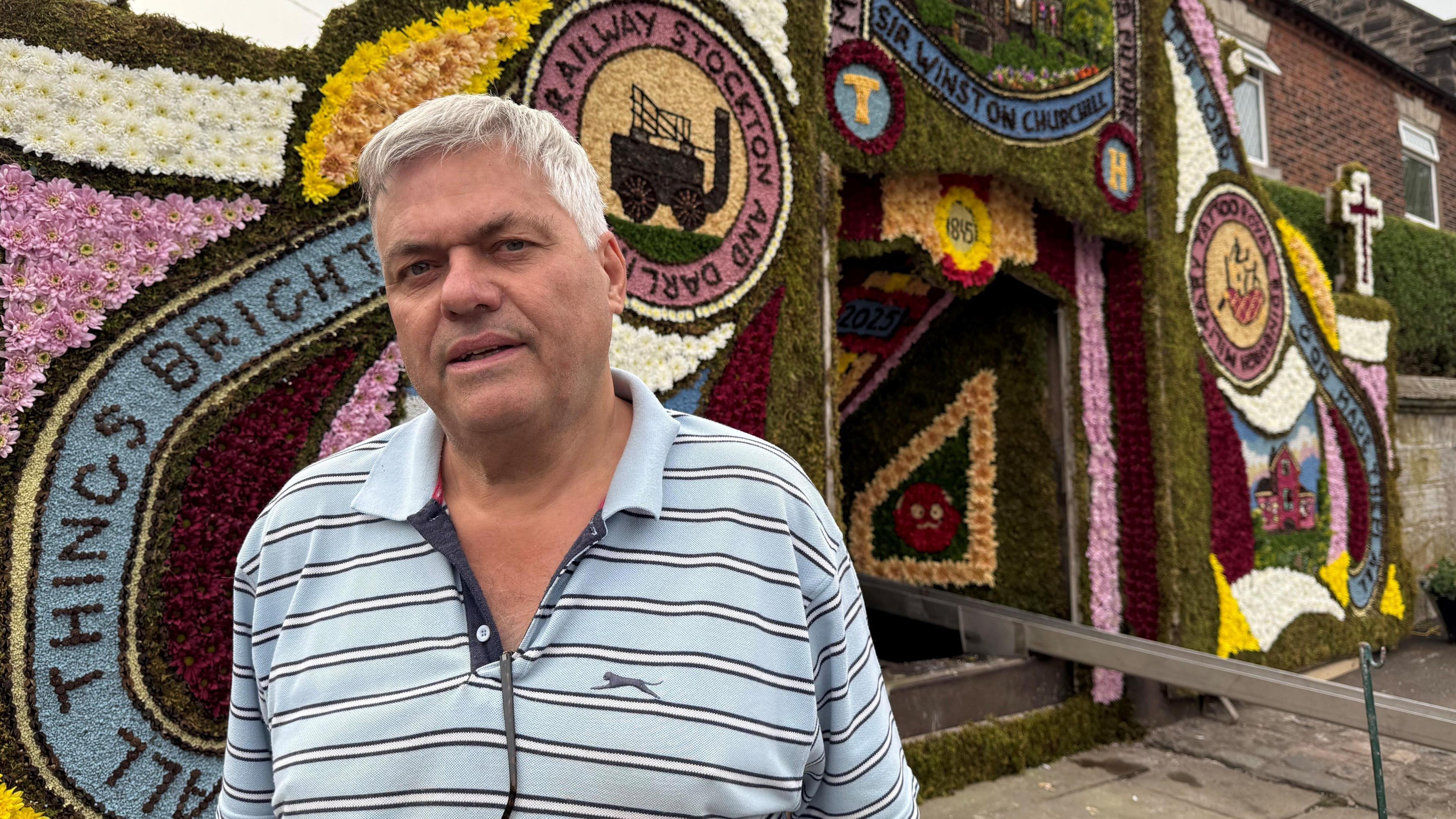 Rob Barlow, stood next to the decorated well in Endon. He is wearing a striped blue top.