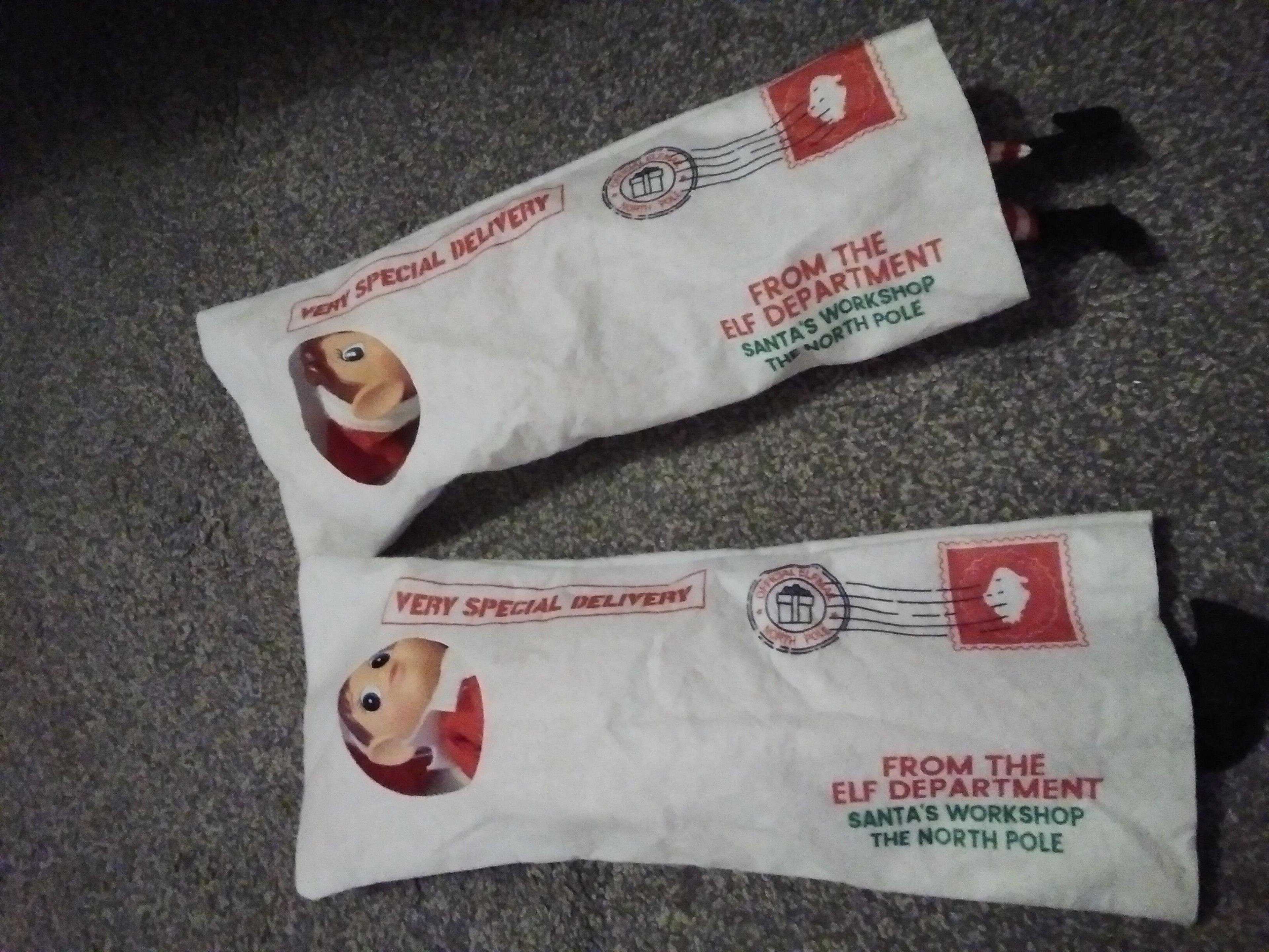 Two plastic elves lie on their back inside cloth pouches shaped like envelopes. the outside reads: "Very special delivery, from the Elf Department, Santa's workshop the North Pole"