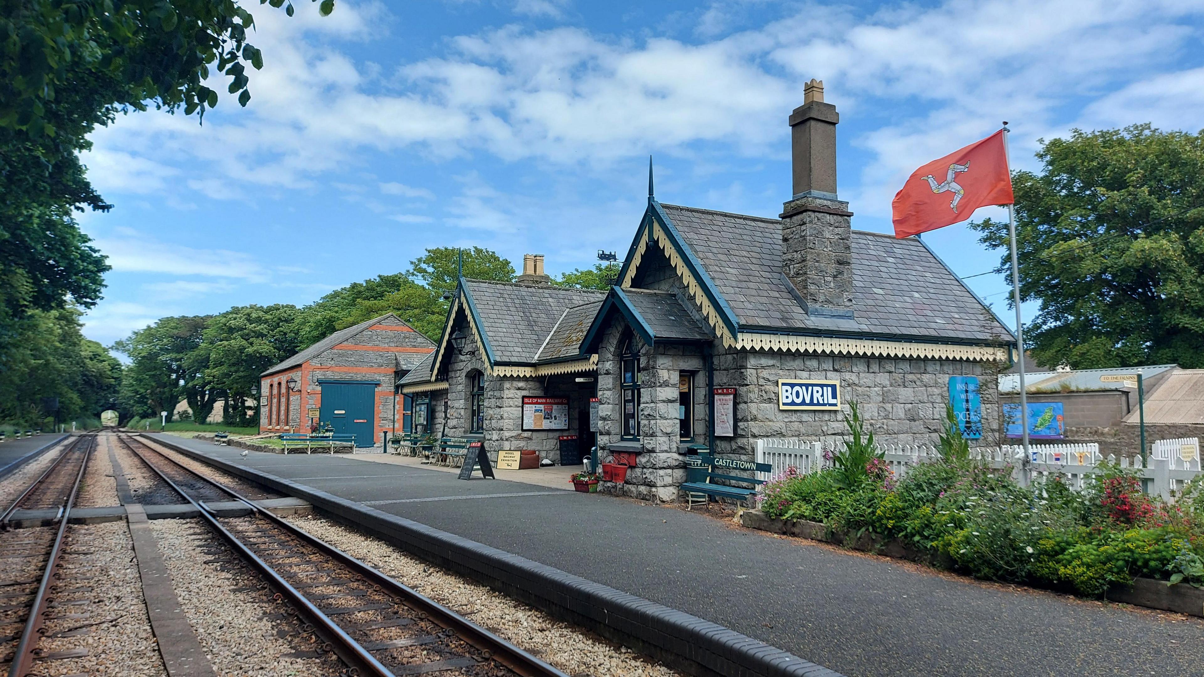 The Castletown Station made of grey stone, comprises two buildings, with railway lines in front of it.