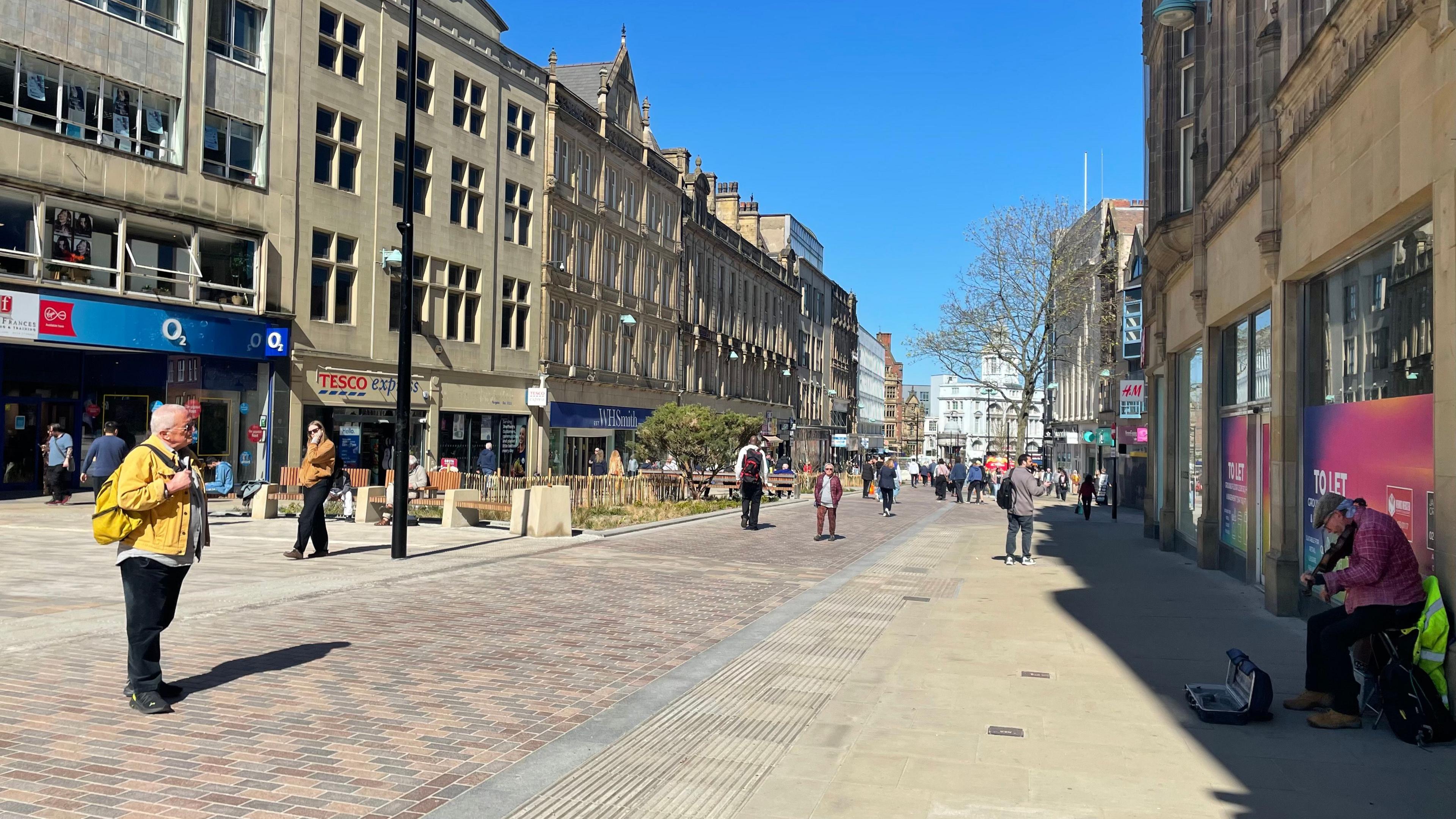 A view over Fargate, an open space with shops lining either side of the street and benches in the middle of the walkway.