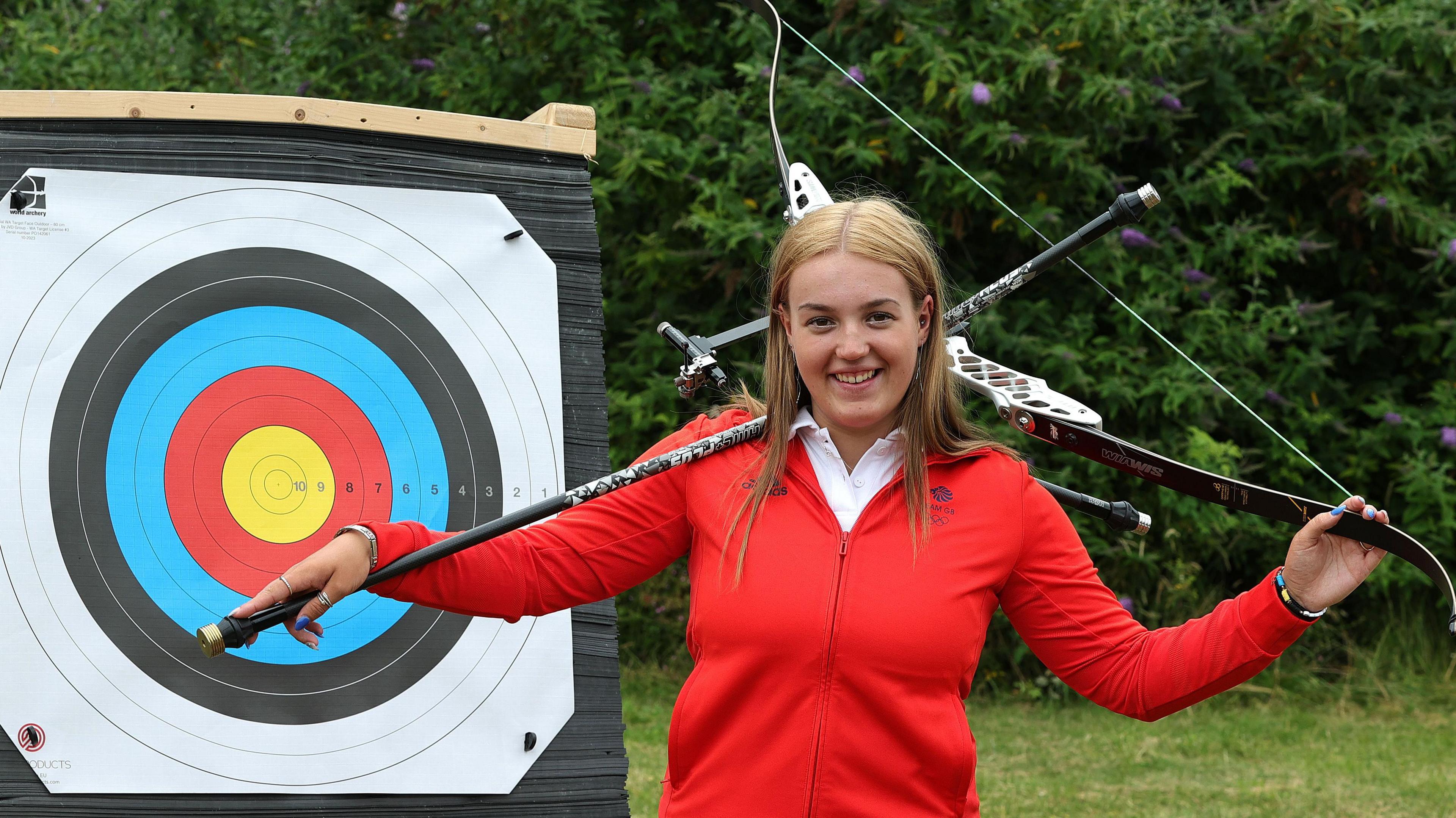 Megan Havers holding bow and arrow posing in front of target