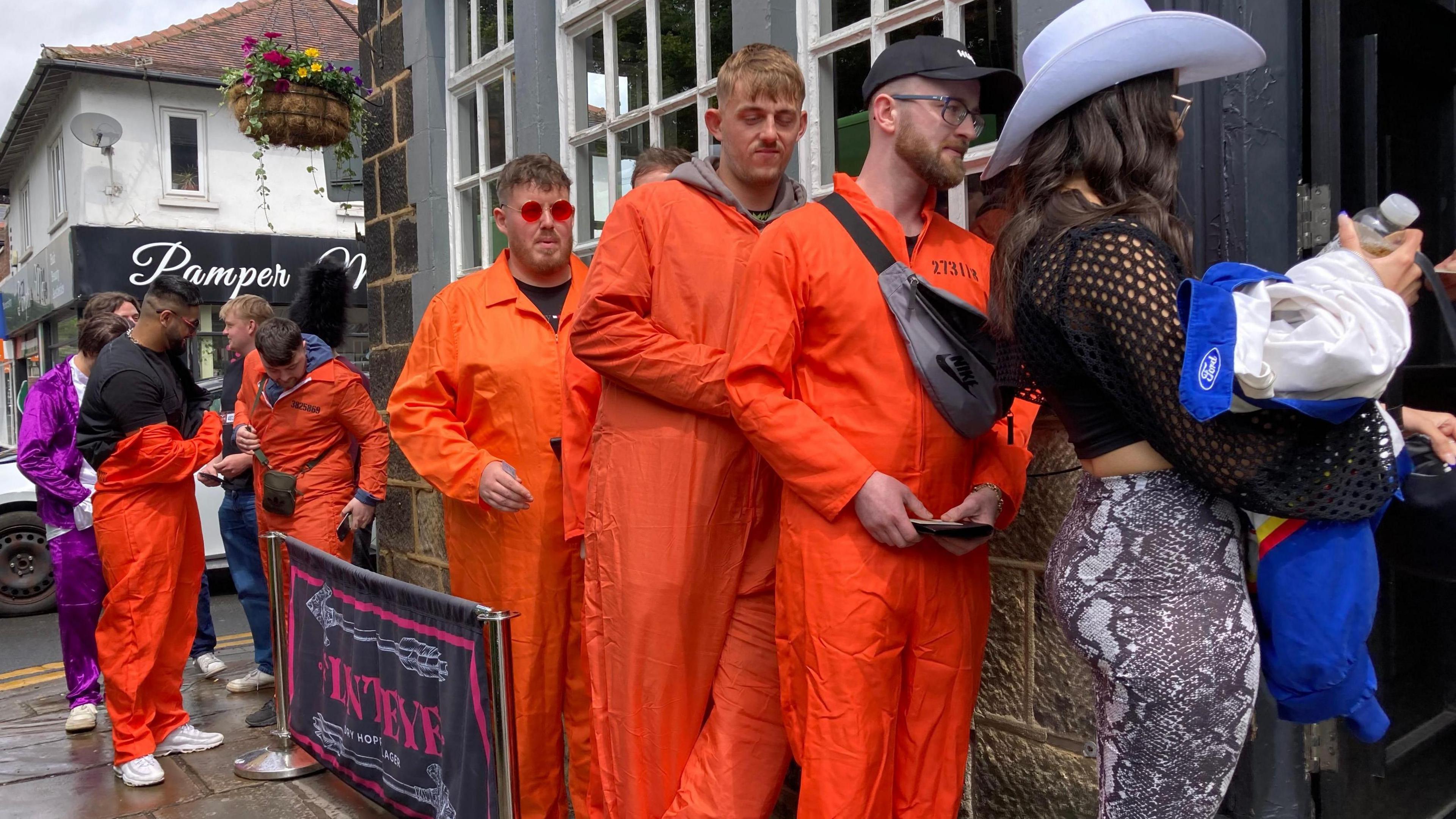 Several people wearing fancy dress queue to get in a pub.
