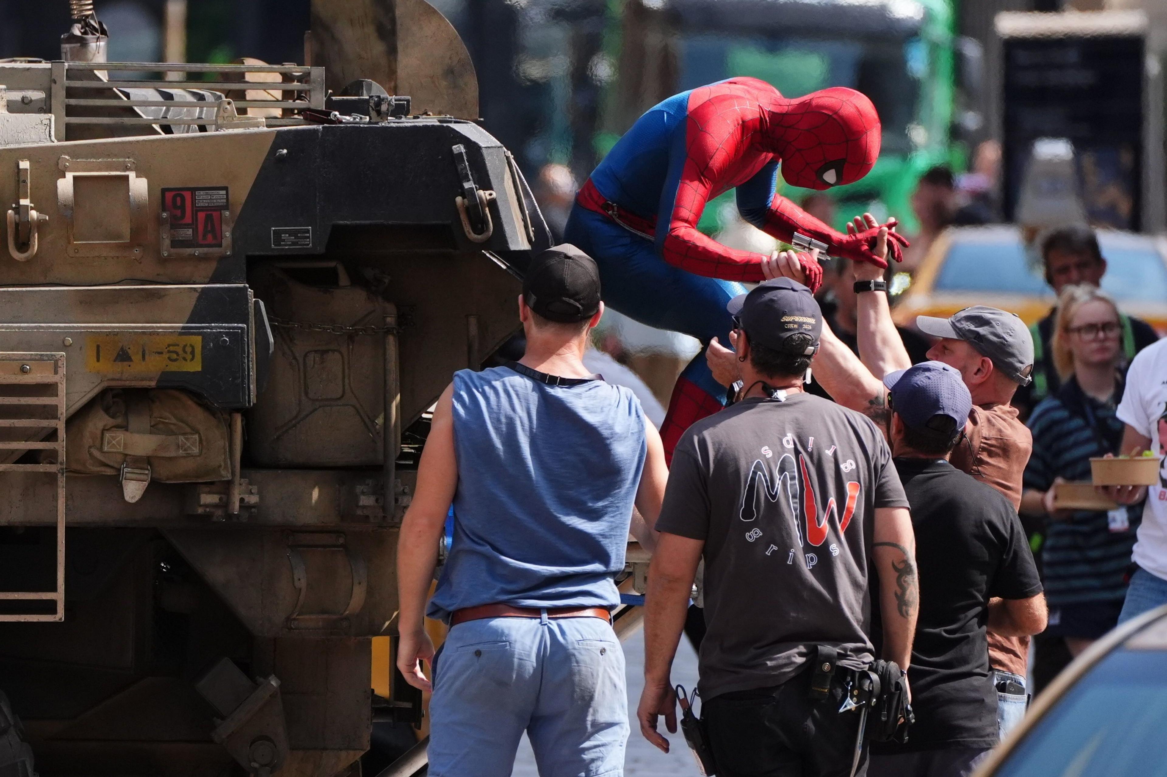 A person in a Spider-Man suit is helped down from a tank during filming.