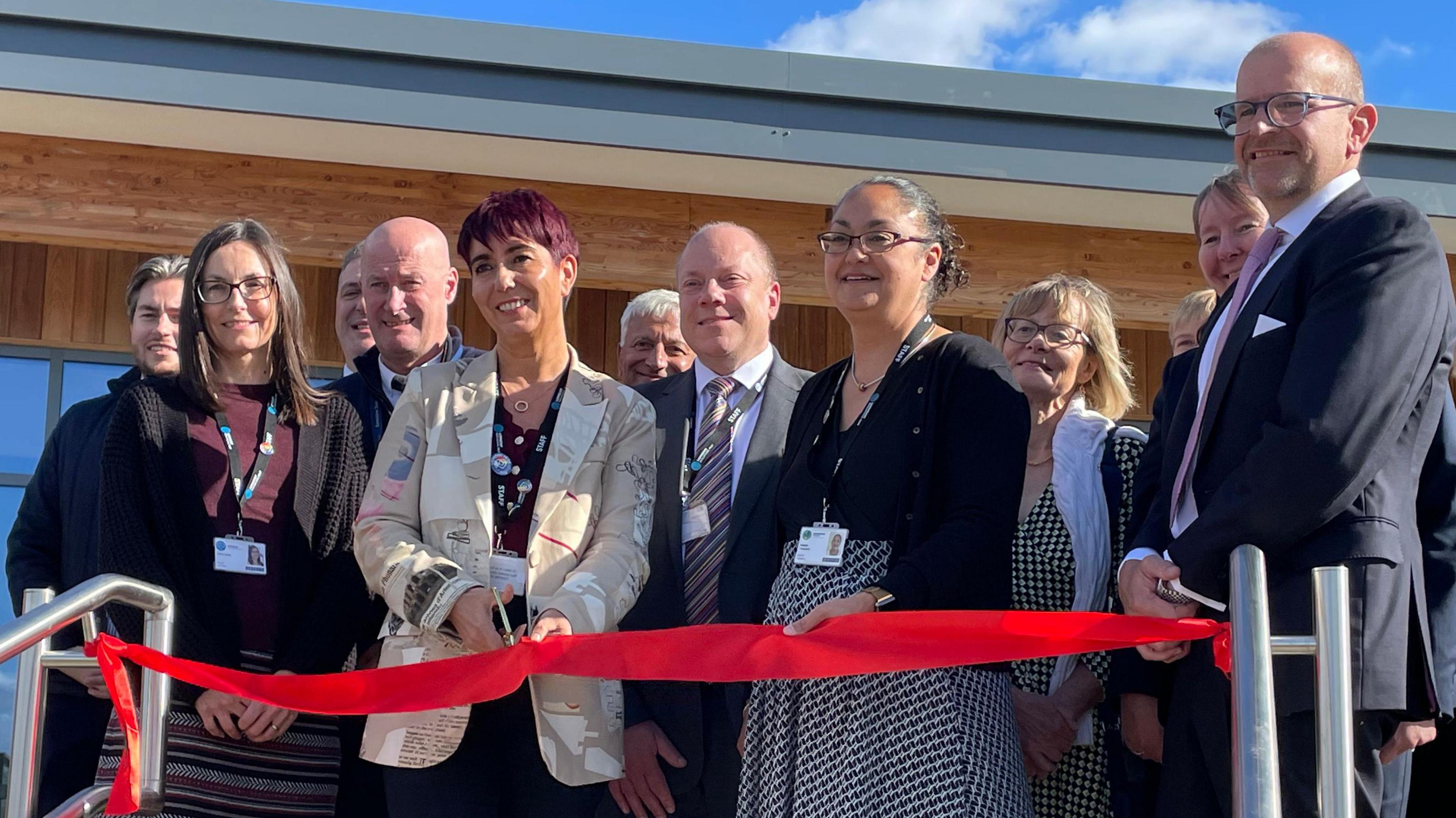 The ribbon cutting ceremony with dignitaries gathered behind a red ribbon with some shiny scissors being brandished