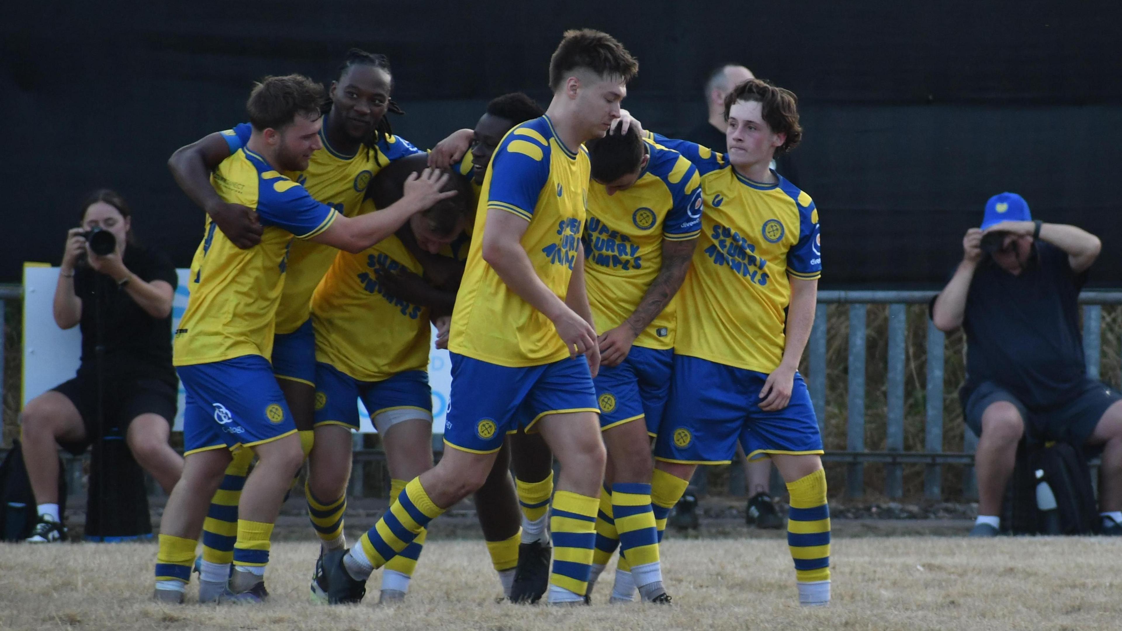 Members of the men's Cwmbran AFC side gathered together on the pitch during the game. The kit is blue and yellow with super furry animals written on the front