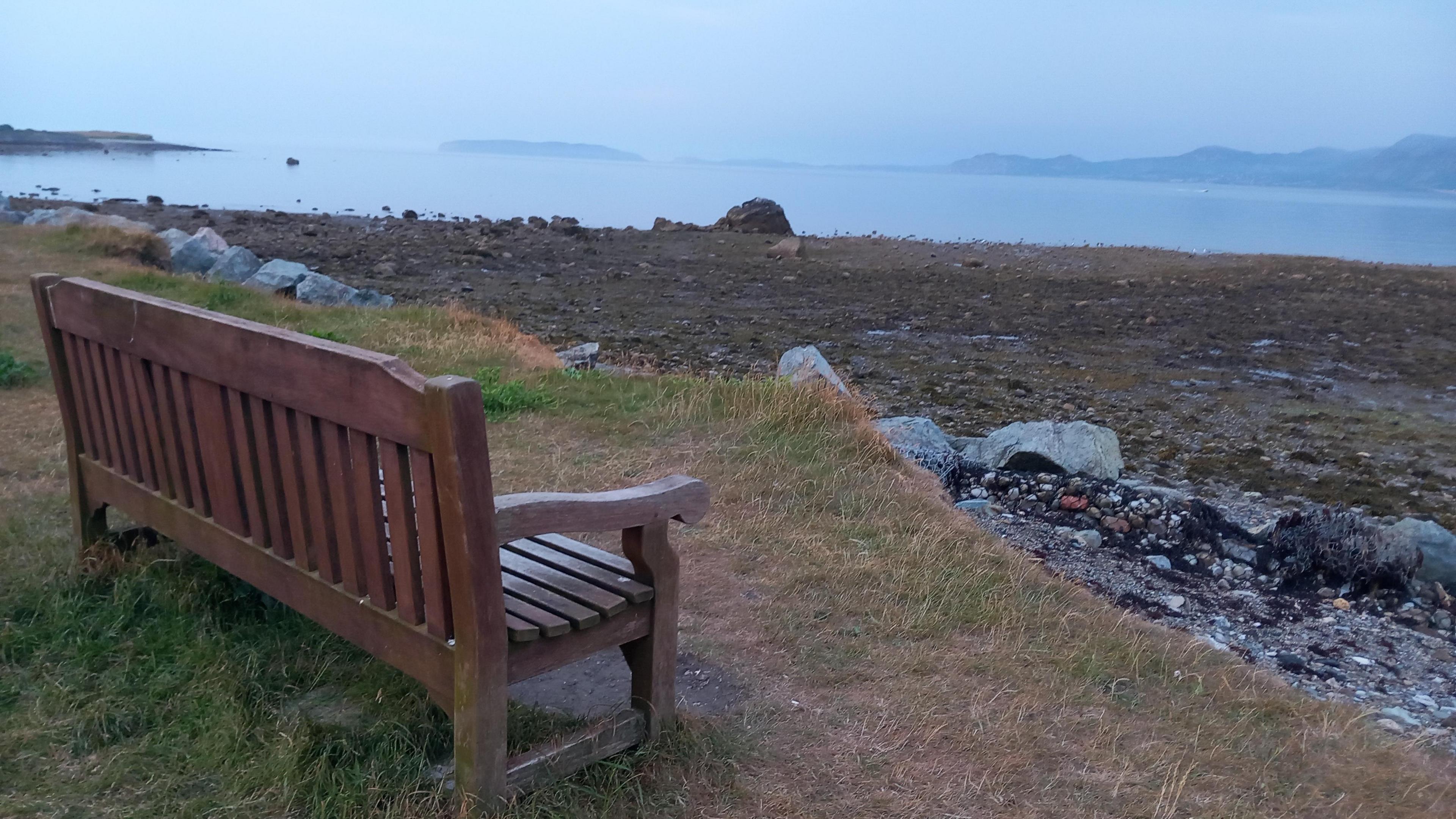 A bench looking out at the sea with mountains in the backgorund