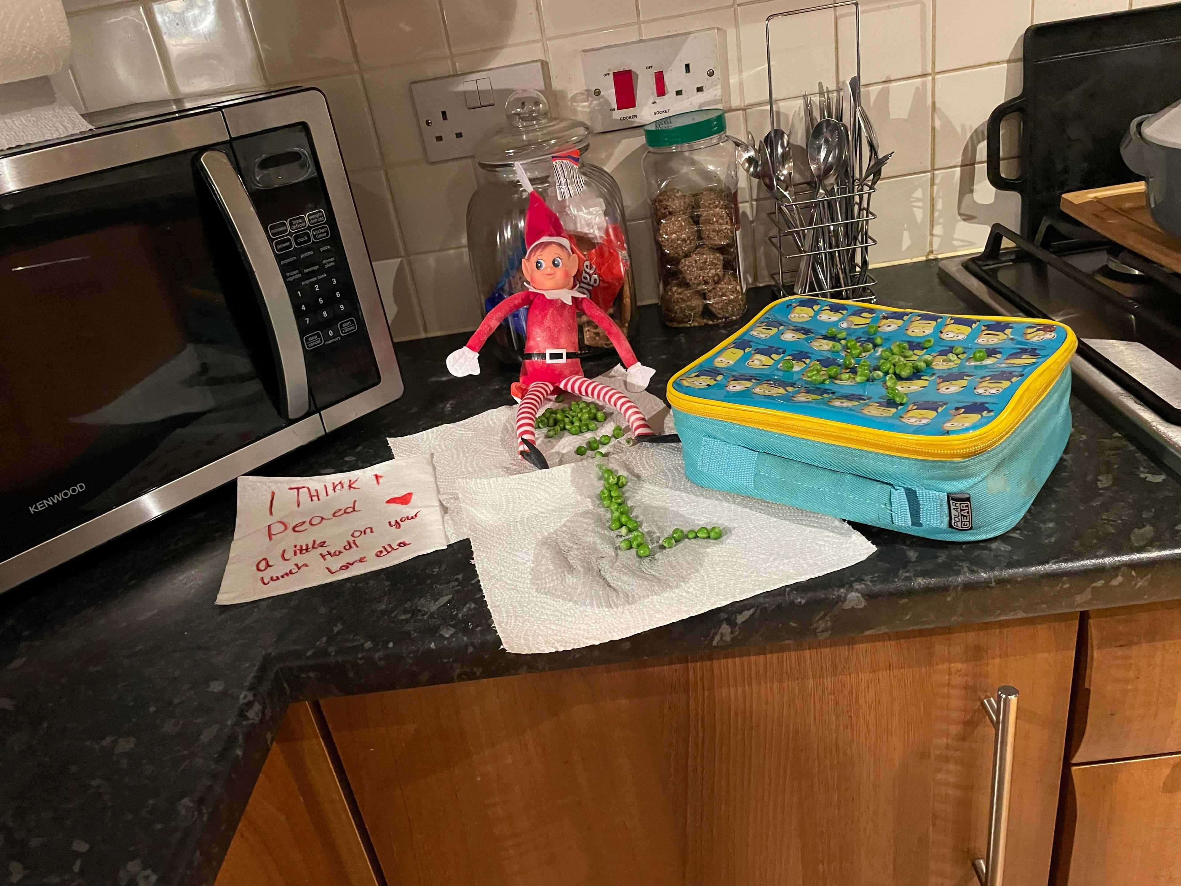 An elf sits on a kitchen counter with peas. 