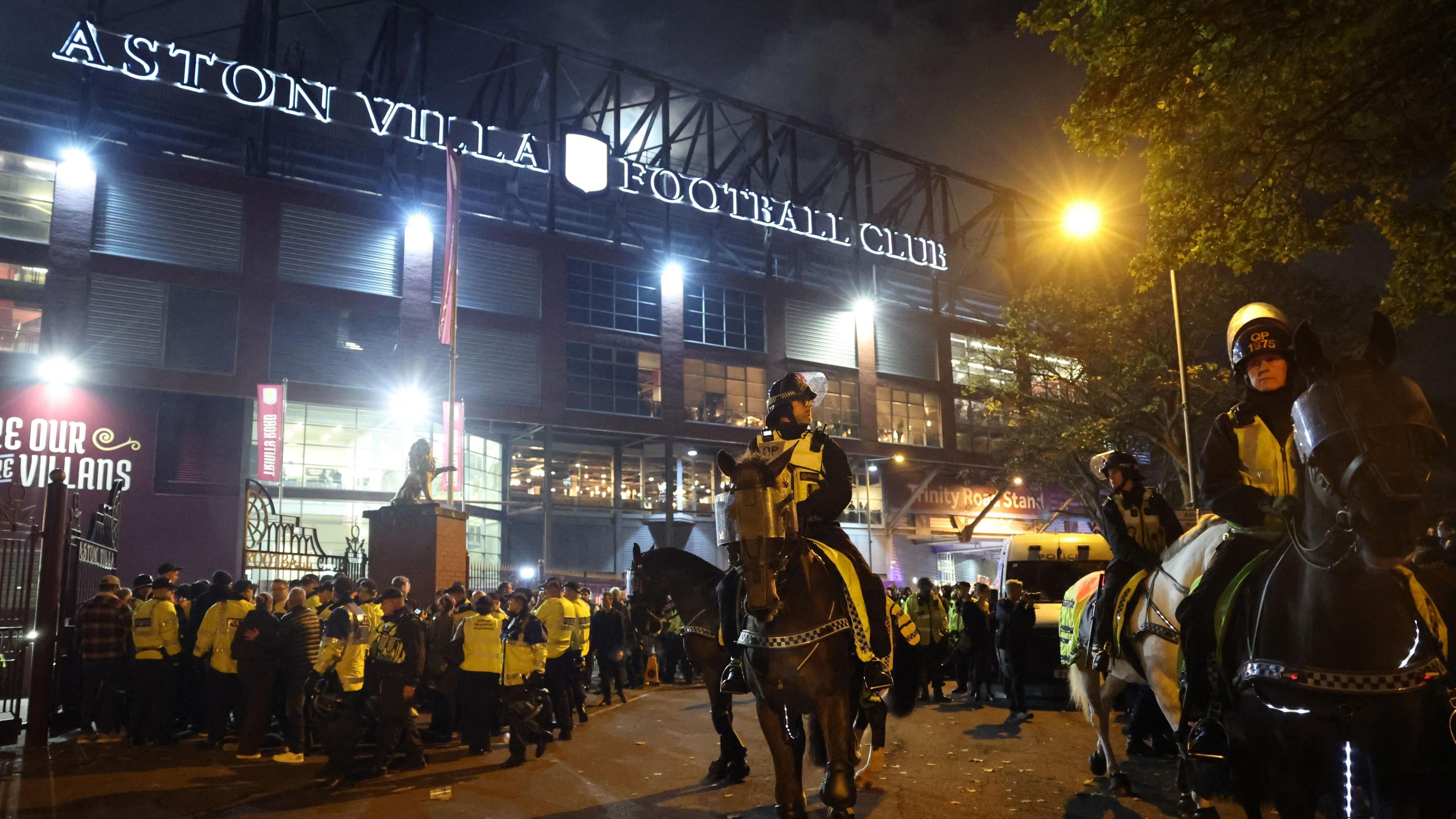 Mounted police officers wearing high-vis jackets over uniform stand outside Aston Villa Football ground. Behind them many other officers wearing bright yellow jackets can be seen 